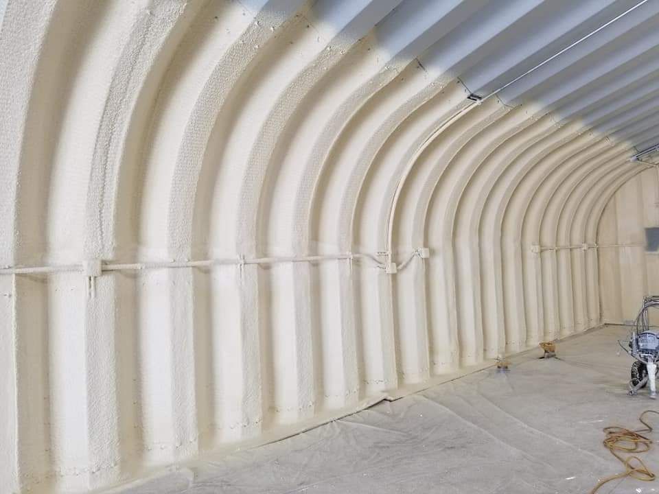 Insulated interior of a curved metal building. Light-colored foam insulation covers the arched walls.