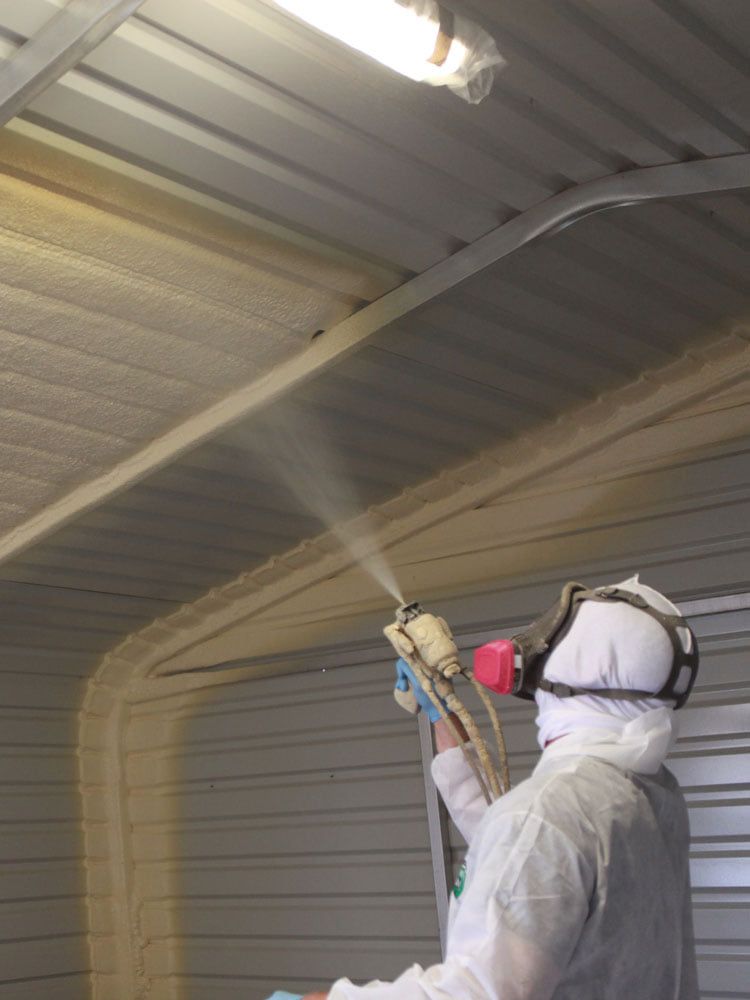Person spraying insulation on a metal ceiling; protective gear worn.