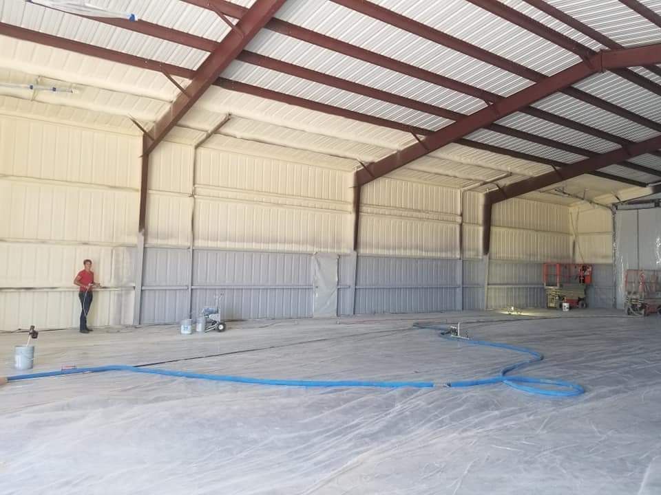 Interior of a warehouse with spray foam insulation. A person stands near a blue hose on the concrete floor.