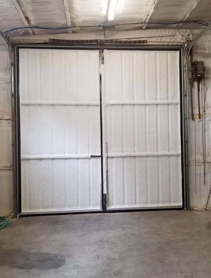 White, corrugated metal double doors in a concrete room with black metal framing and a lever handle.