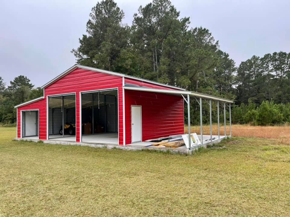 Red metal barn with open bays, lean-to, and a red roof, set in a grassy field, under an overcast sky.