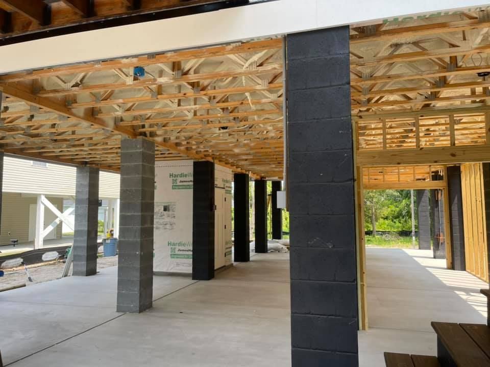 Under-construction building with concrete pillars supporting a wooden floor, with a view to outside greenery.