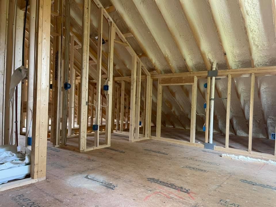 Interior framing of a building under construction, spray foam insulation visible, unfinished wood surfaces.