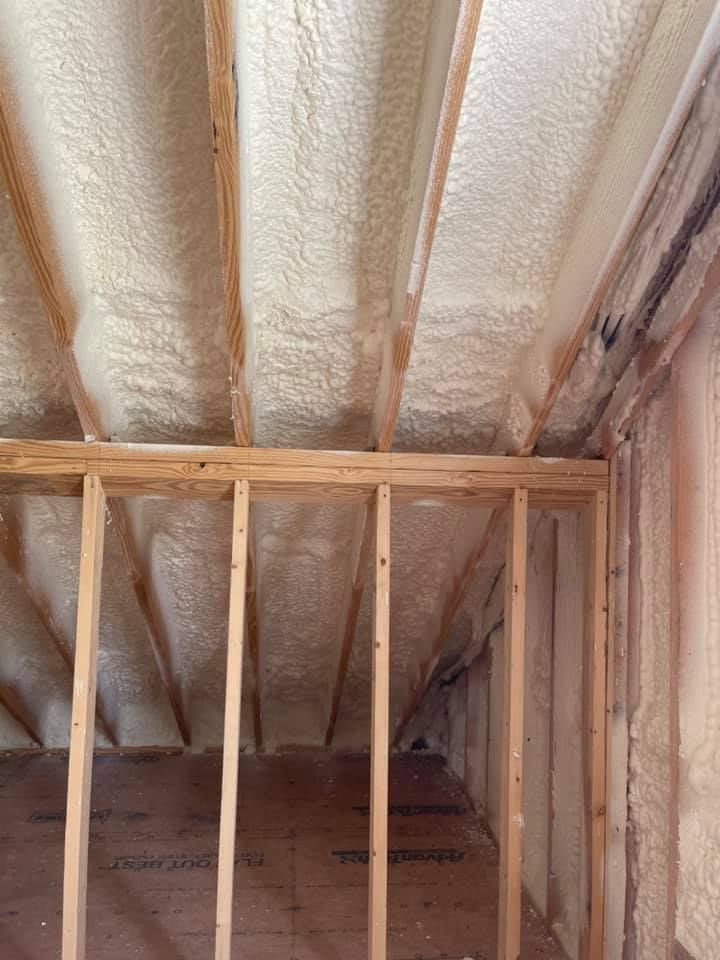 Spray foam insulation on ceiling and walls of unfinished room with exposed wooden beams and framing.