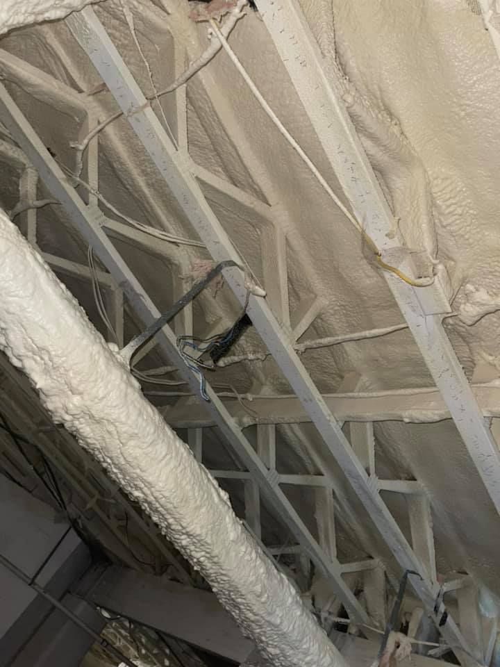 Spray foam insulation on ceiling beams in an attic, with wiring visible.