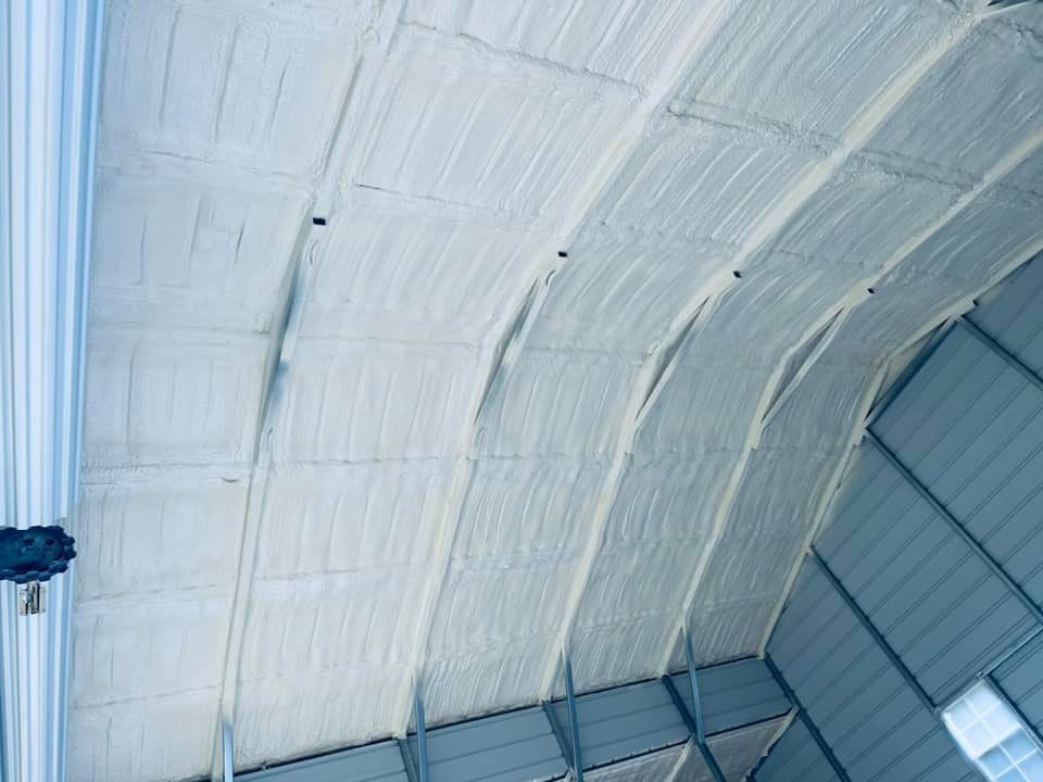 White spray foam insulation covering a curved metal roof structure.