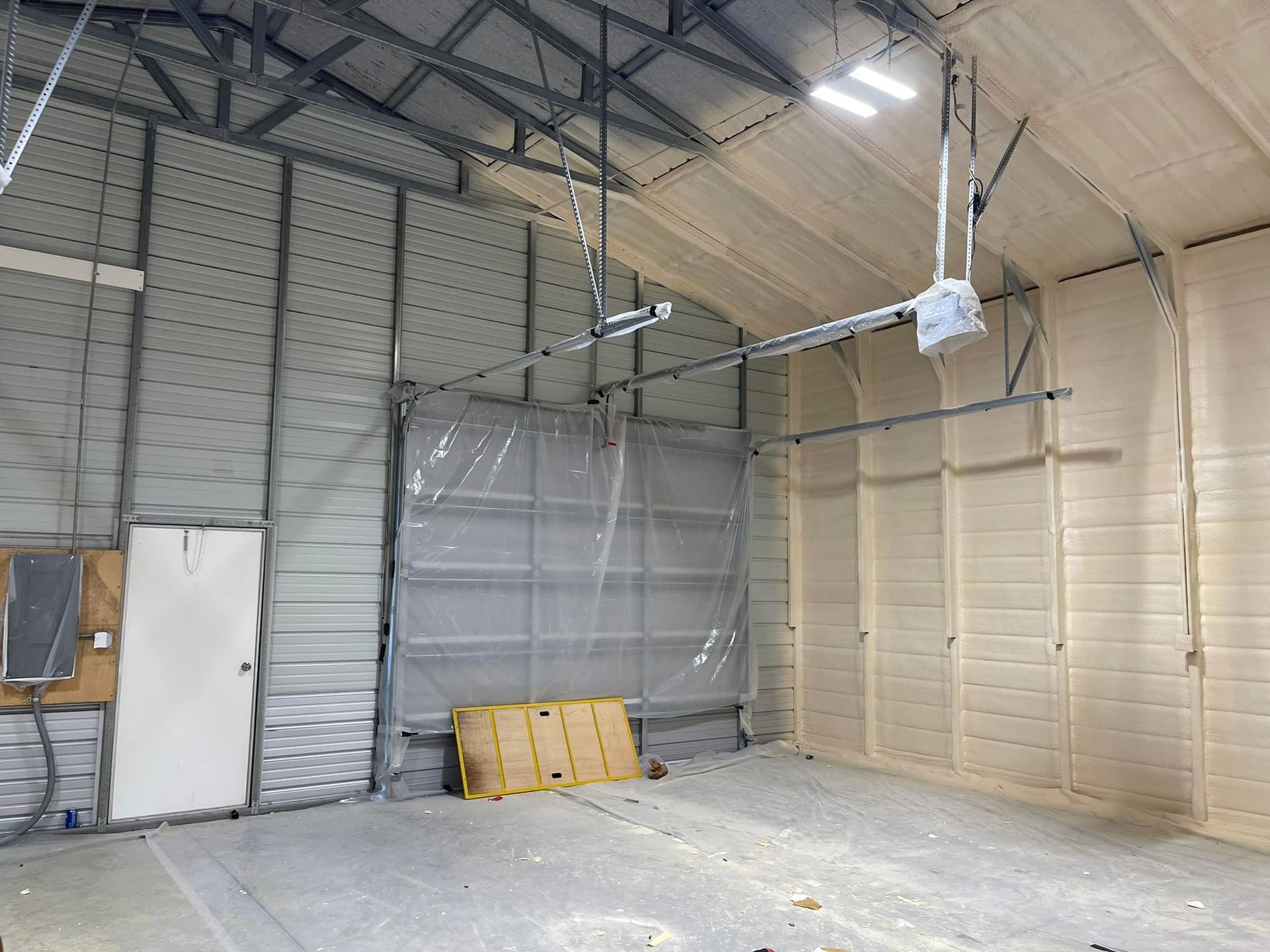 Interior of a metal building with garage door, white door, and spray foam insulation.