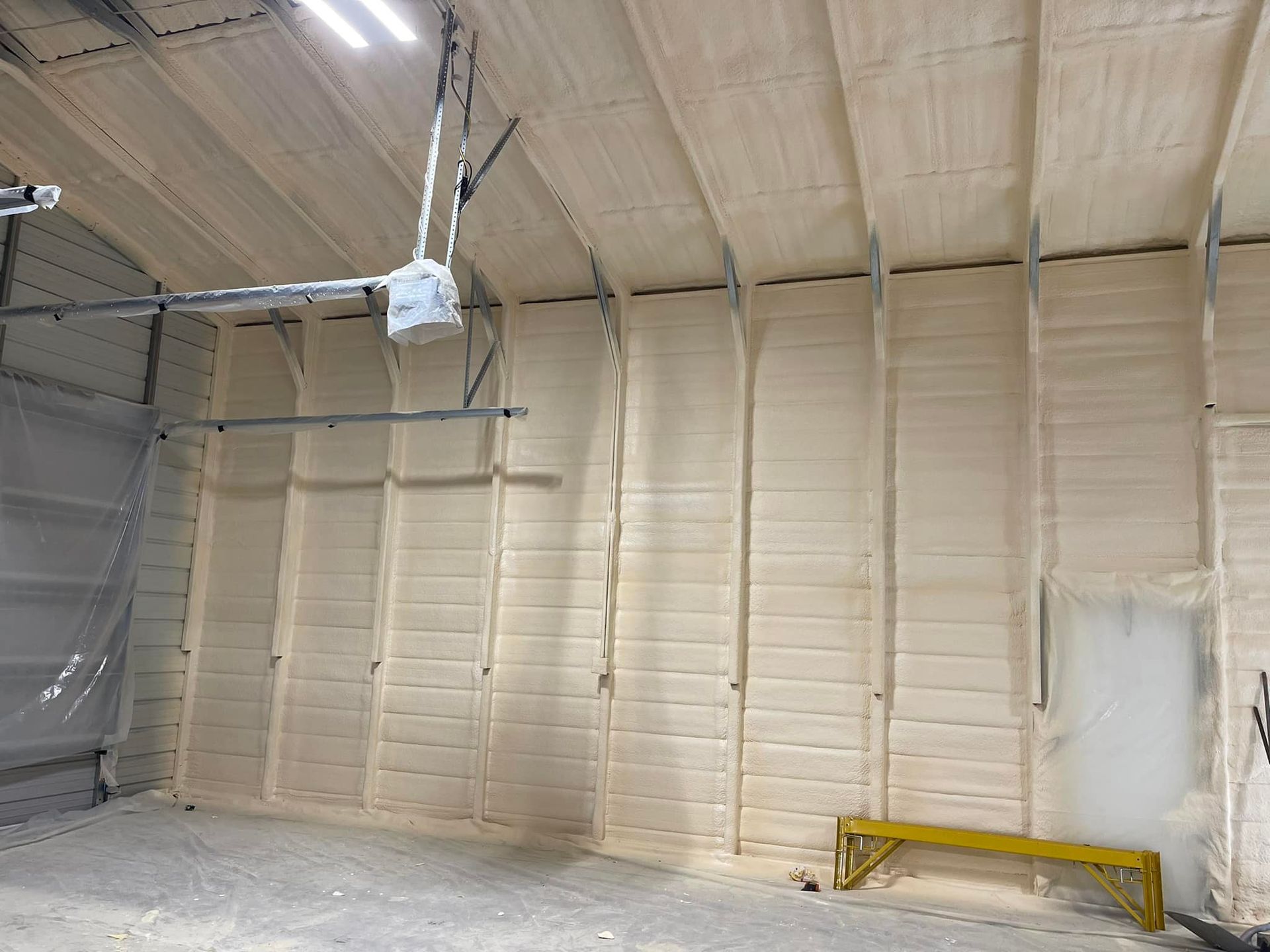 Spray foam insulation covering the walls and ceiling of a building. A yellow bench is in the foreground.