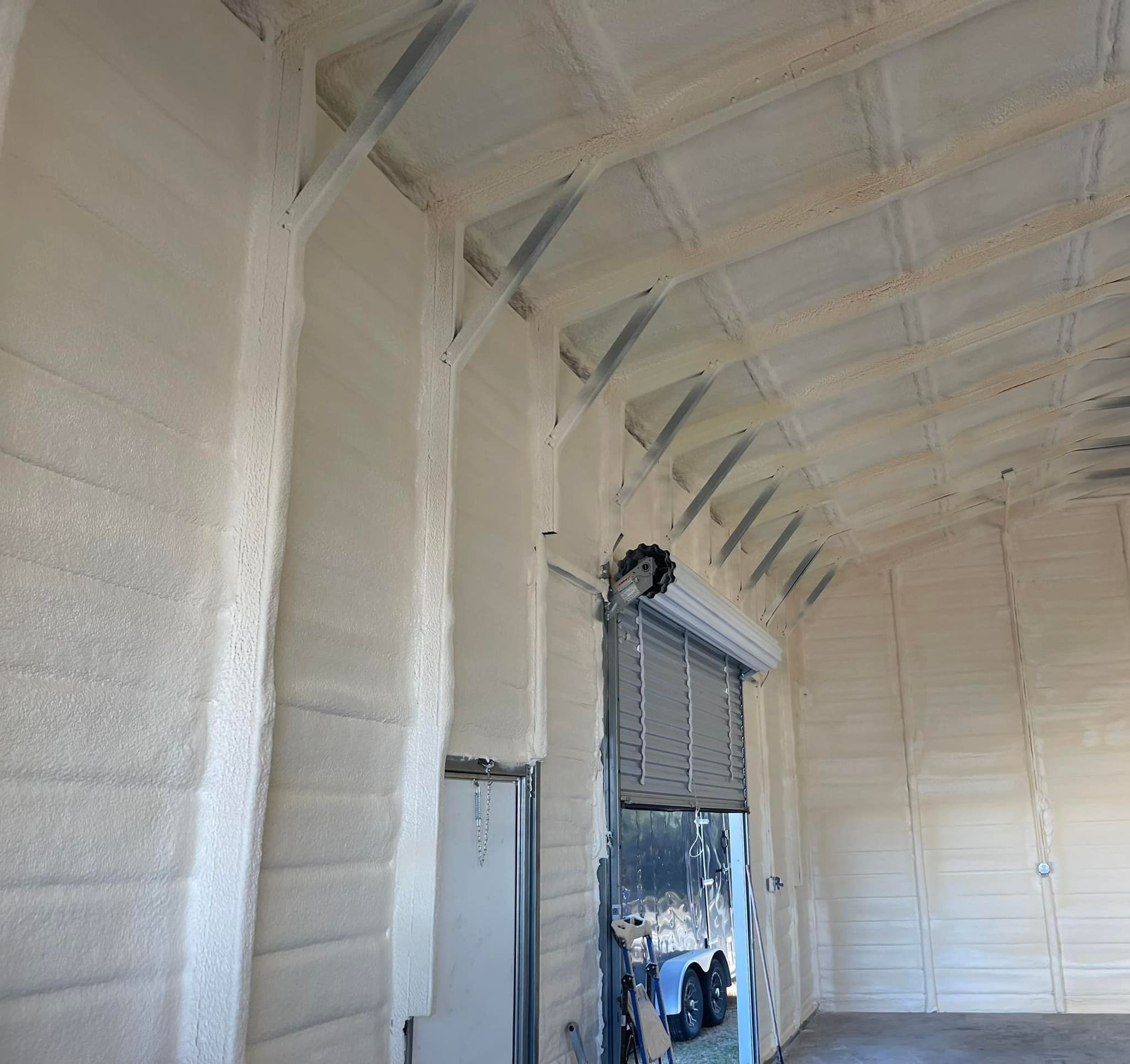 Interior of a building with spray foam insulation on walls and ceiling, including a closed roll-up door.