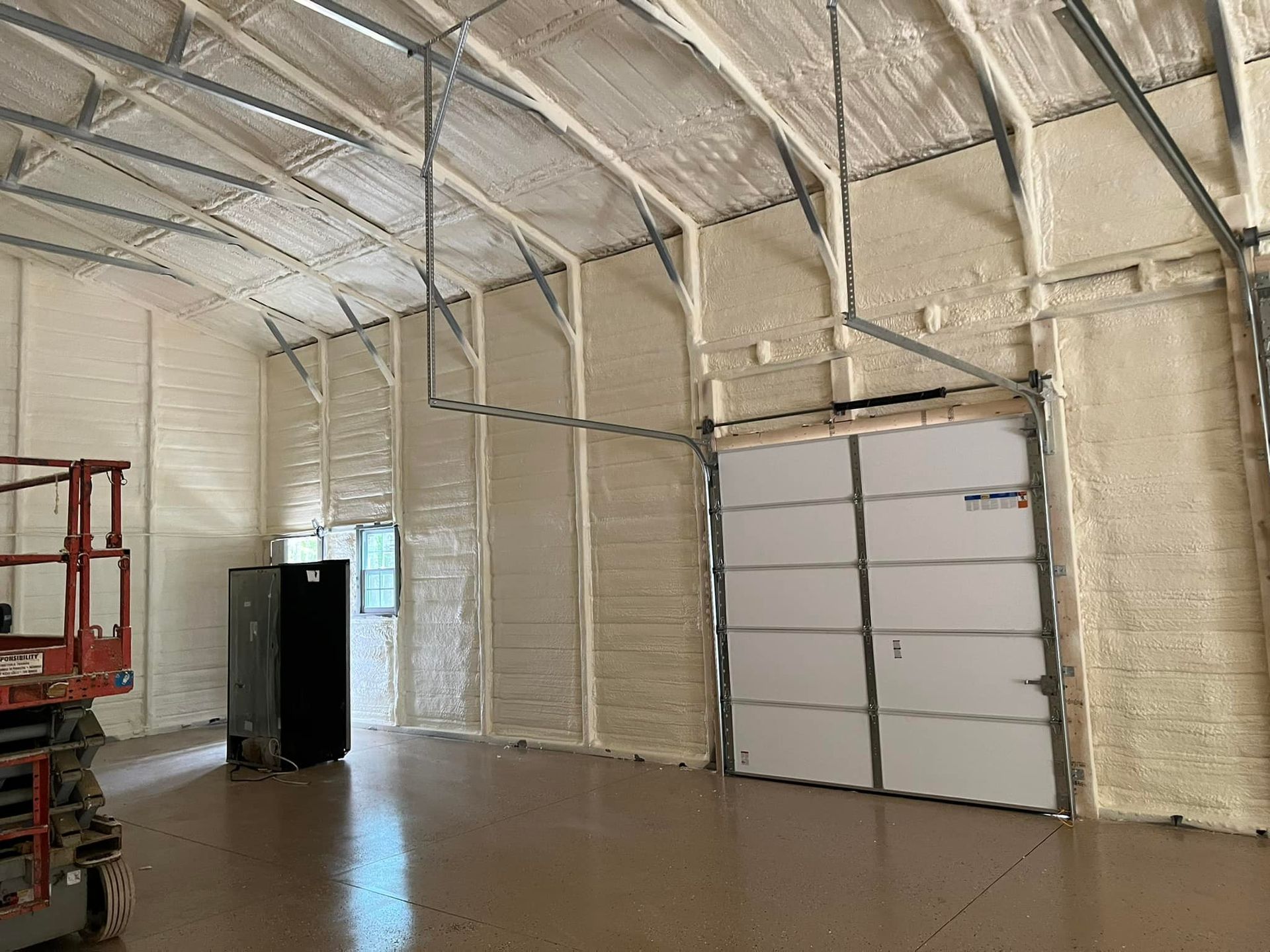 Interior view of a building with spray foam insulation on walls and ceiling, a garage door, and a lift.