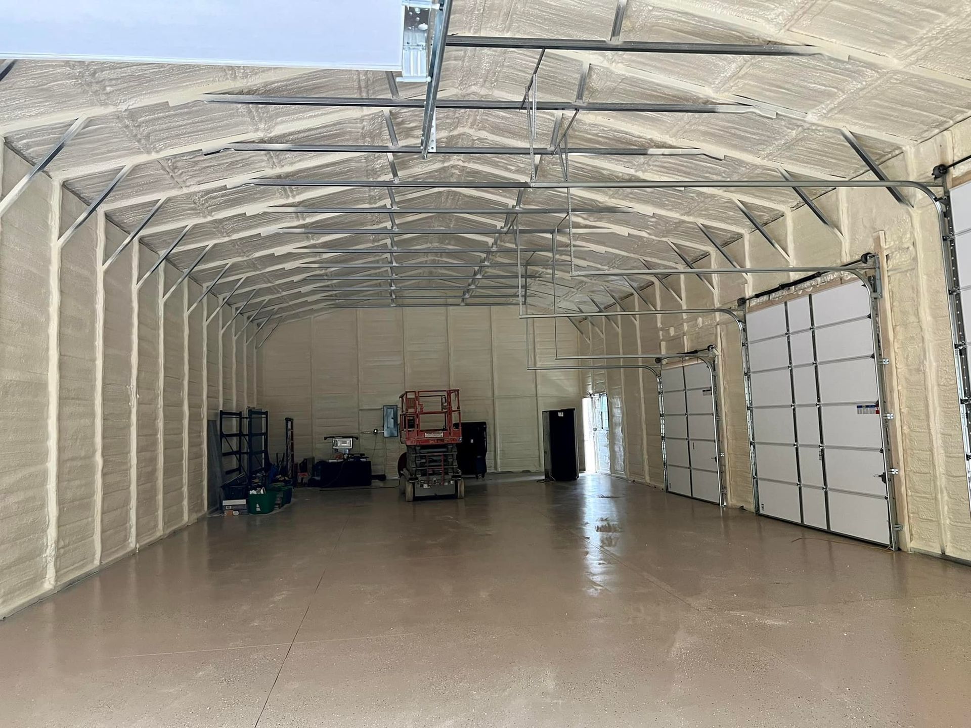 Interior of a large warehouse with spray foam insulation, metal beams, and large garage doors.