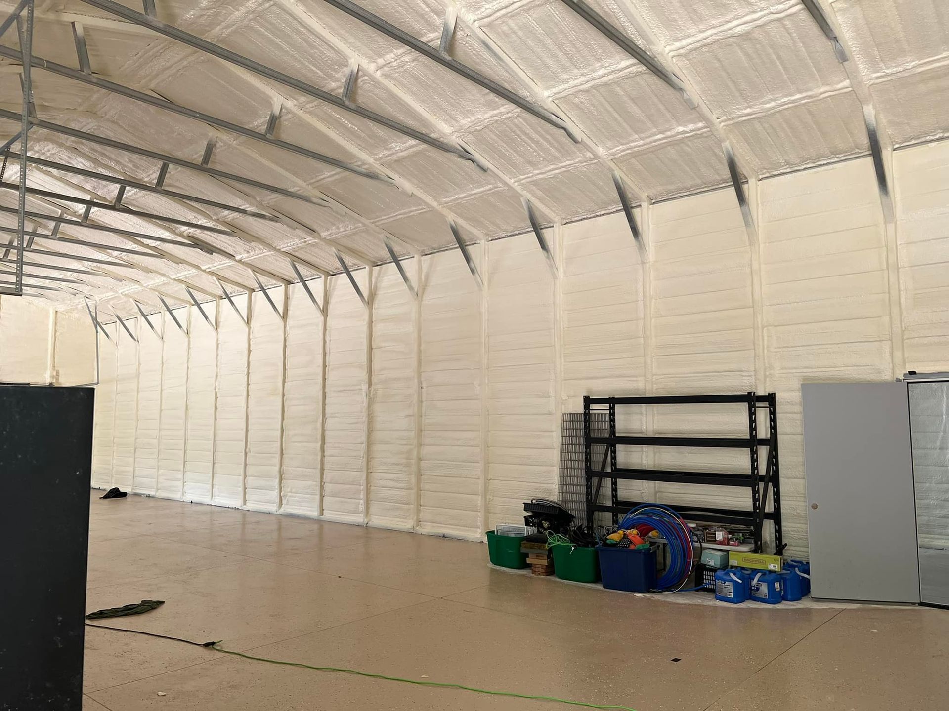 Interior of a large building with arched ceiling and walls insulated with spray foam. Some storage items are visible.