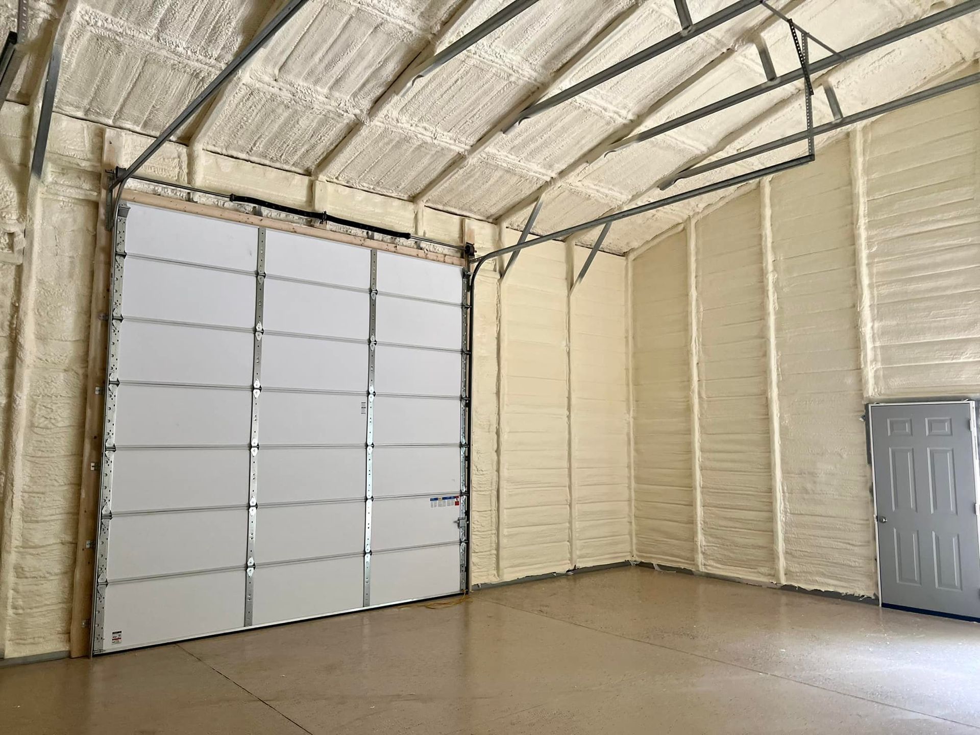 Interior of a warehouse with a large closed garage door, insulated walls and ceiling.
