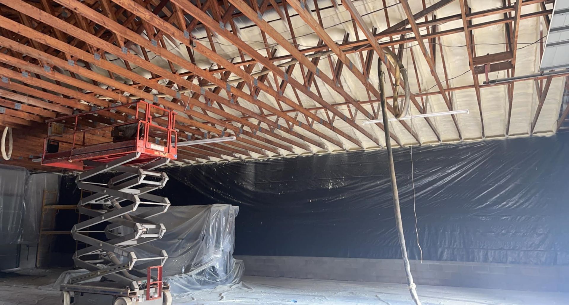 Interior view of construction site with a scissor lift near exposed ceiling beams. Black tarp covers a wall.