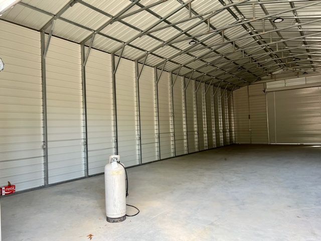 Interior of a large metal building with a concrete floor, a propane tank, and white corrugated walls.