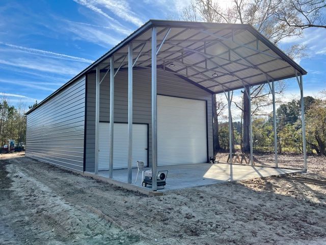Gray metal storage building with an attached carport under a blue sky.