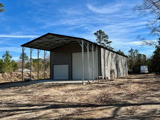 Metal storage building with a partially covered front, on a dirt lot under a blue sky.