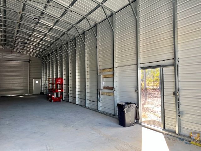 Interior of a metal warehouse. Concrete floor, steel frame, tall walls. Door on right, lift on left.