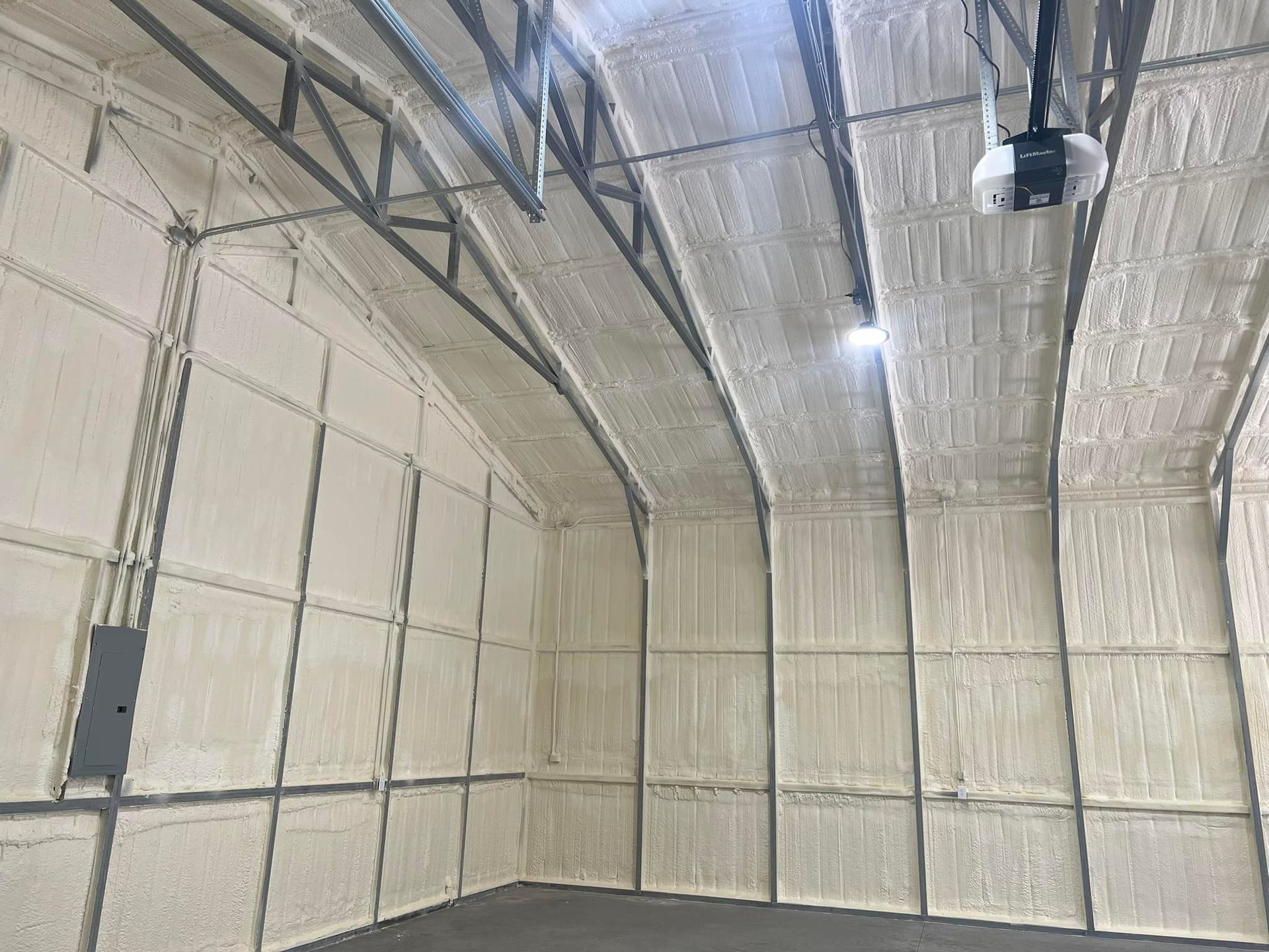 Interior of a metal building with spray foam insulation on walls and ceiling; gray electrical panel on left.