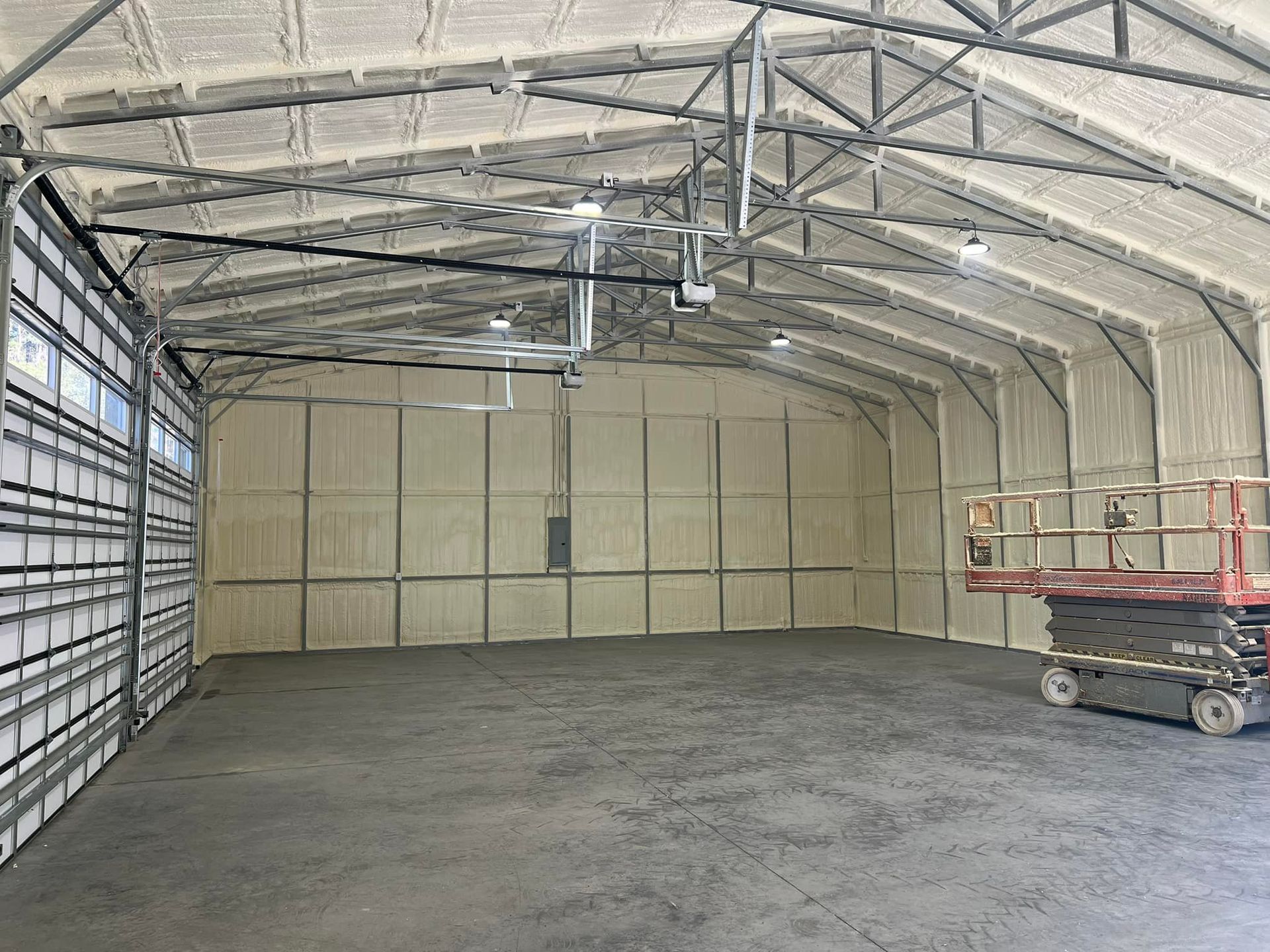 Interior of a large building with spray foam insulation on the walls and ceiling; a closed garage door is visible.