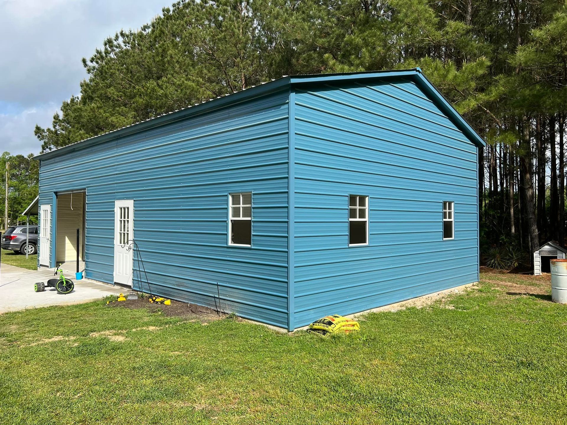 Blue metal building with white doors and windows; set in a grassy yard.