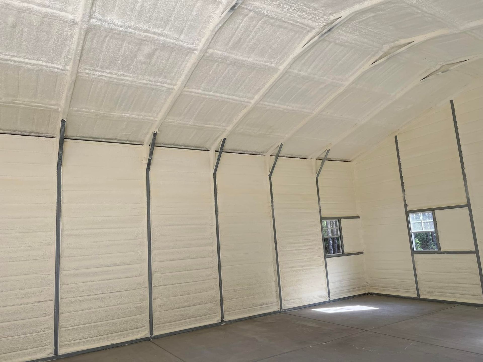 Interior of a building insulated with white foam. Exposed beams and two small windows are visible.