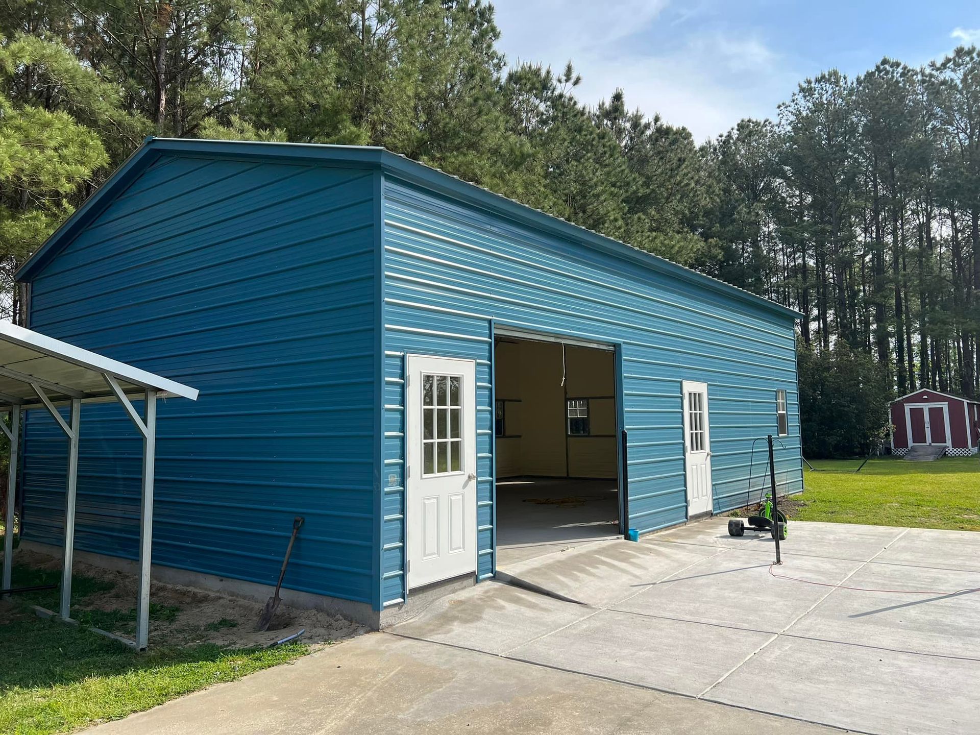 Blue metal building with open garage door, white door, and window; concrete driveway.