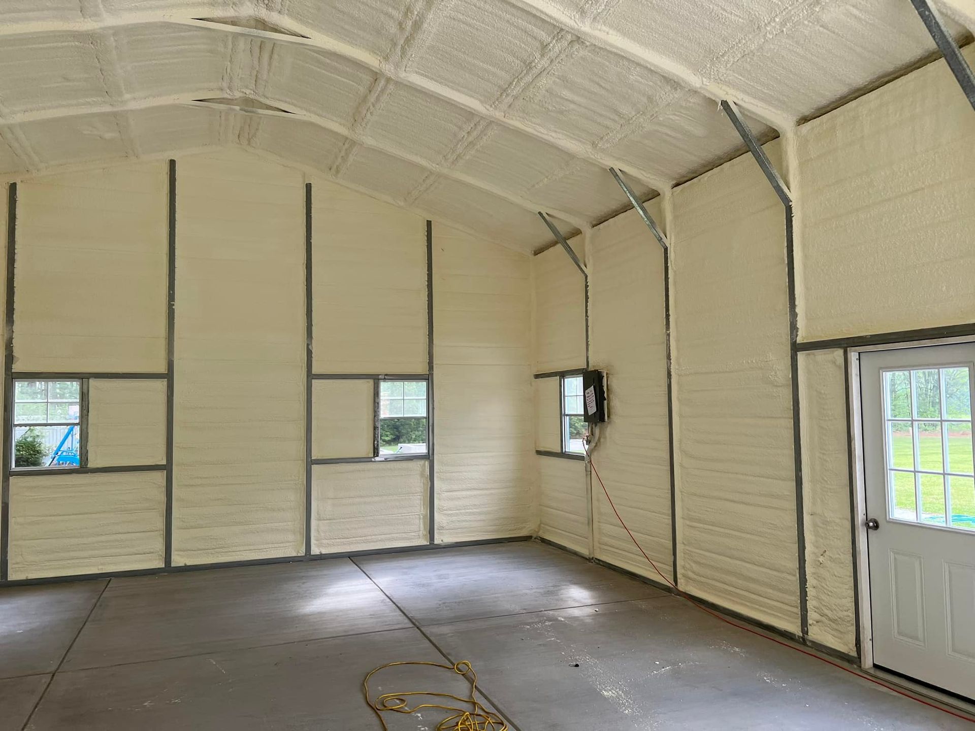 Interior of a building with light-colored spray foam insulation on walls and ceiling, metal beams.