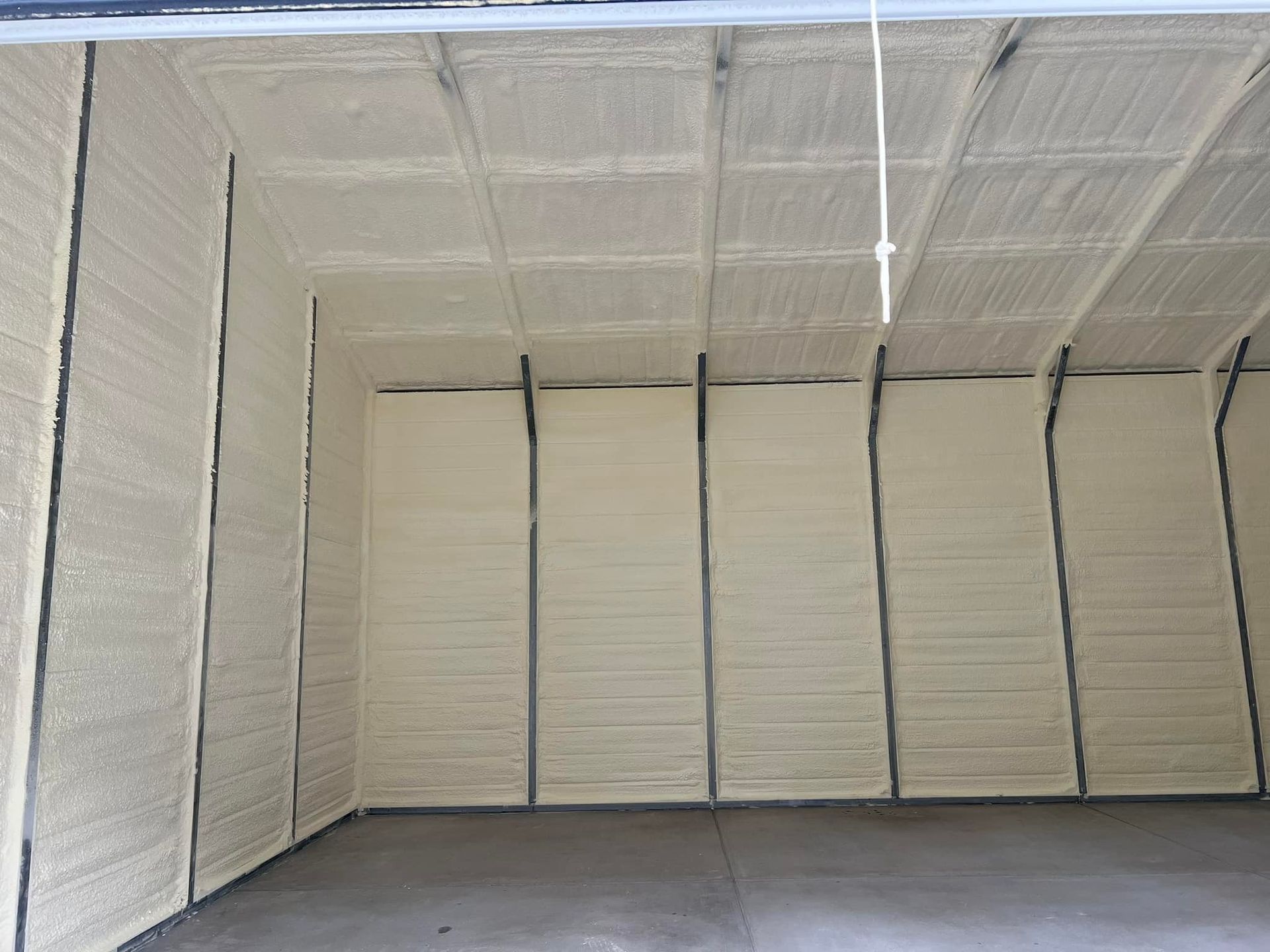 Interior of a structure insulated with light tan spray foam. The walls and ceiling are fully covered.