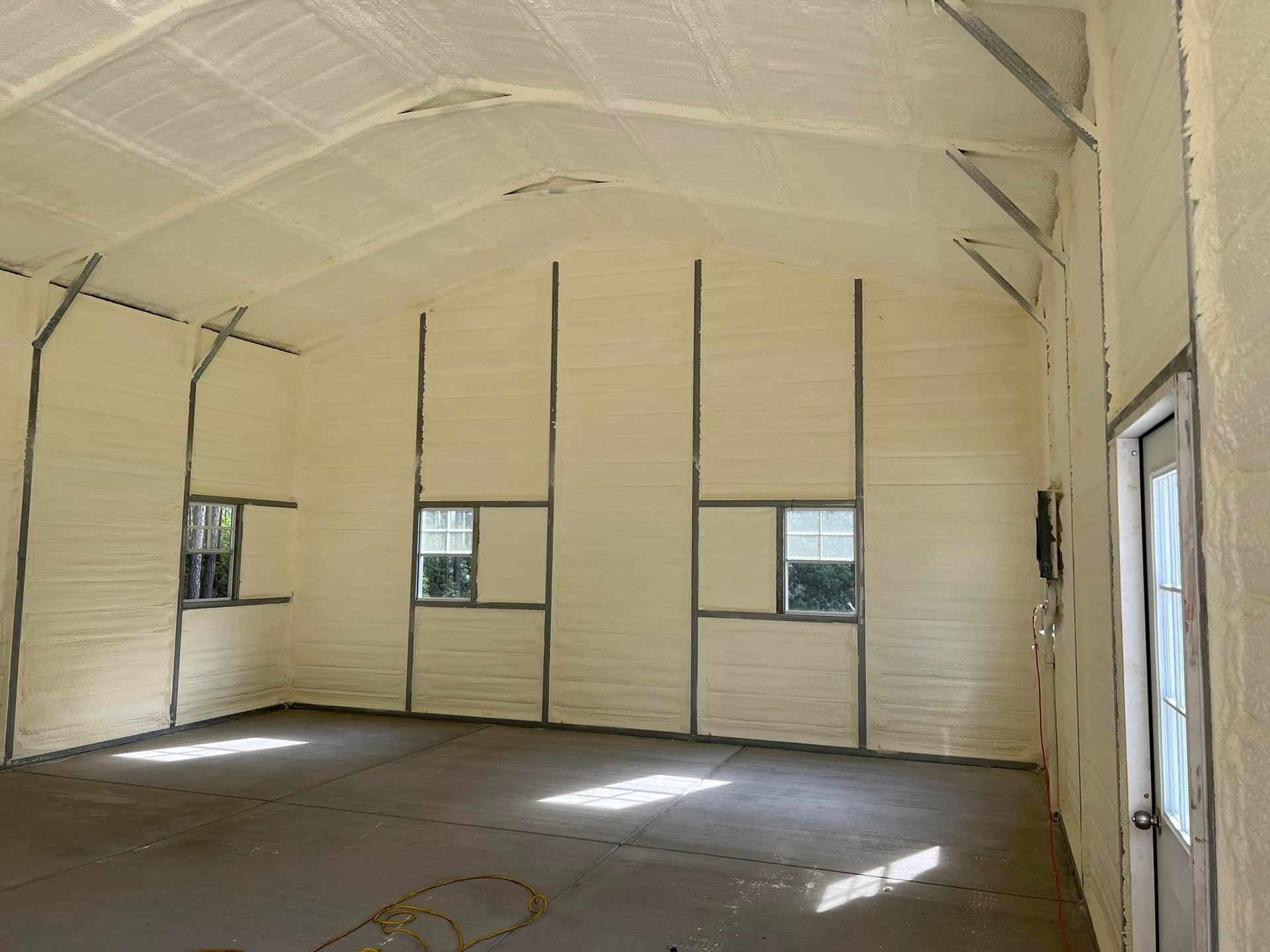 Interior view of a building with spray foam insulation on the walls and ceiling, metal beams, and windows.