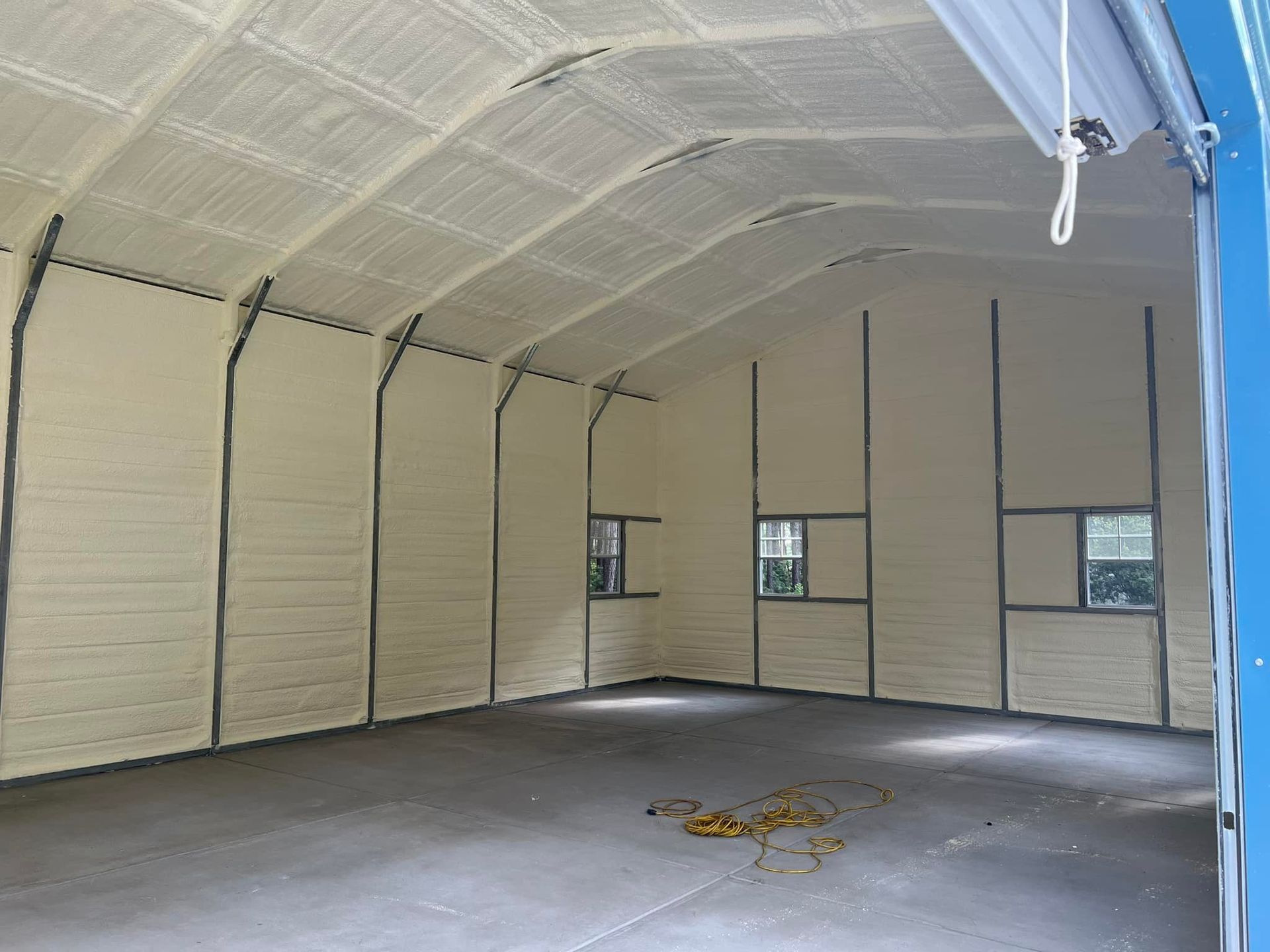 Interior of a large building with spray foam insulation on the walls and ceiling; concrete floor.