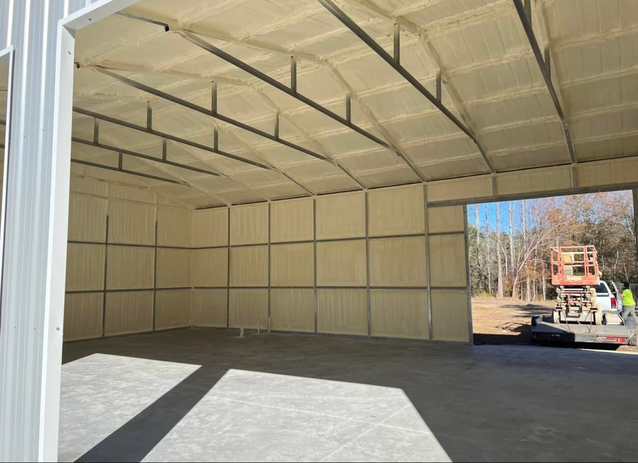 Interior of a metal building with spray foam insulation on walls and ceiling. Concrete floor. Bright sunlight.