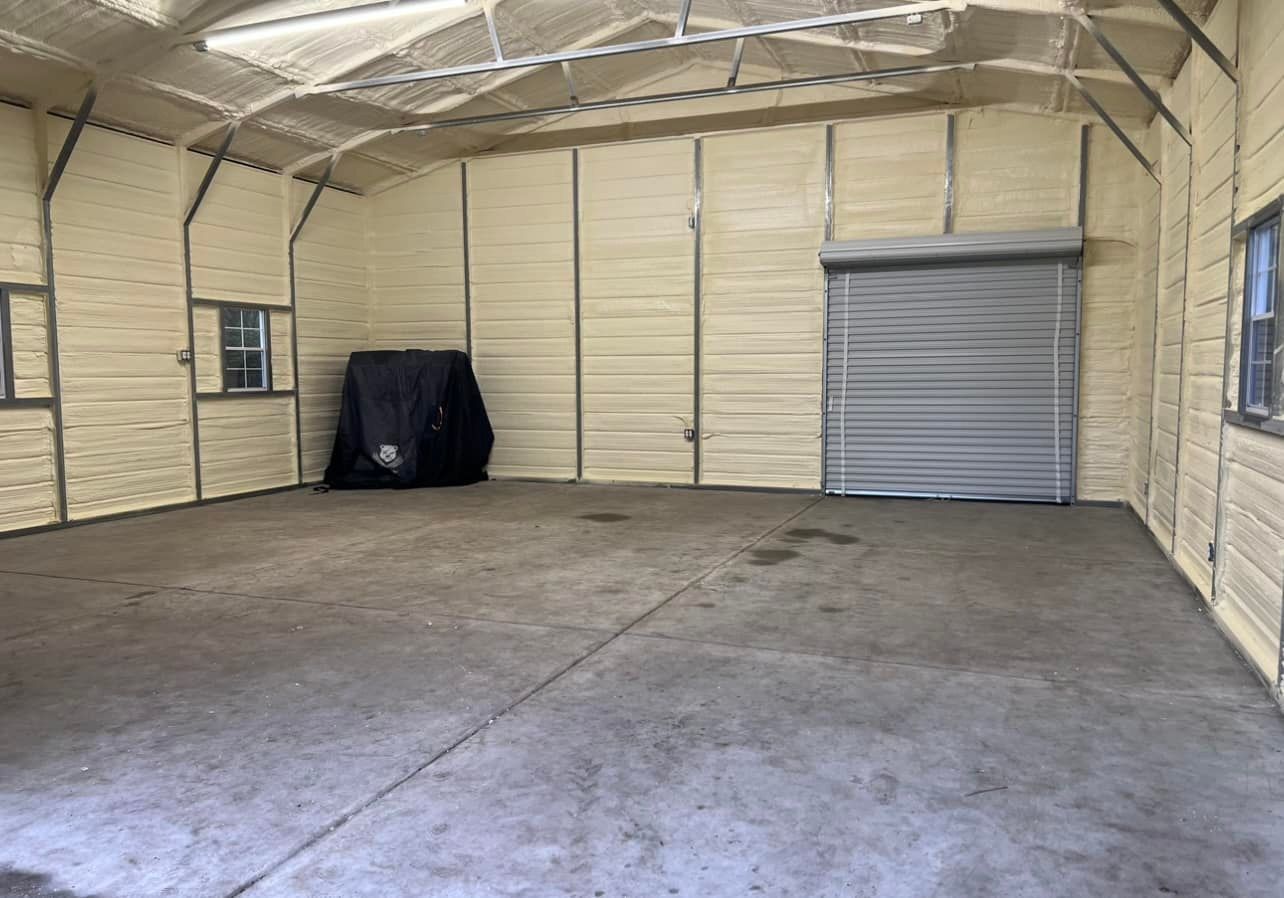 Interior of a tan metal building with a concrete floor, roller door, windows, and exposed metal frame.