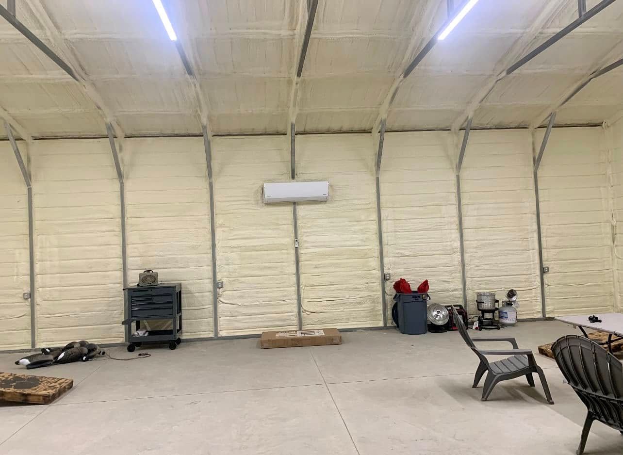 Interior of a large, insulated metal building with a concrete floor, a wood stove, and a few chairs.