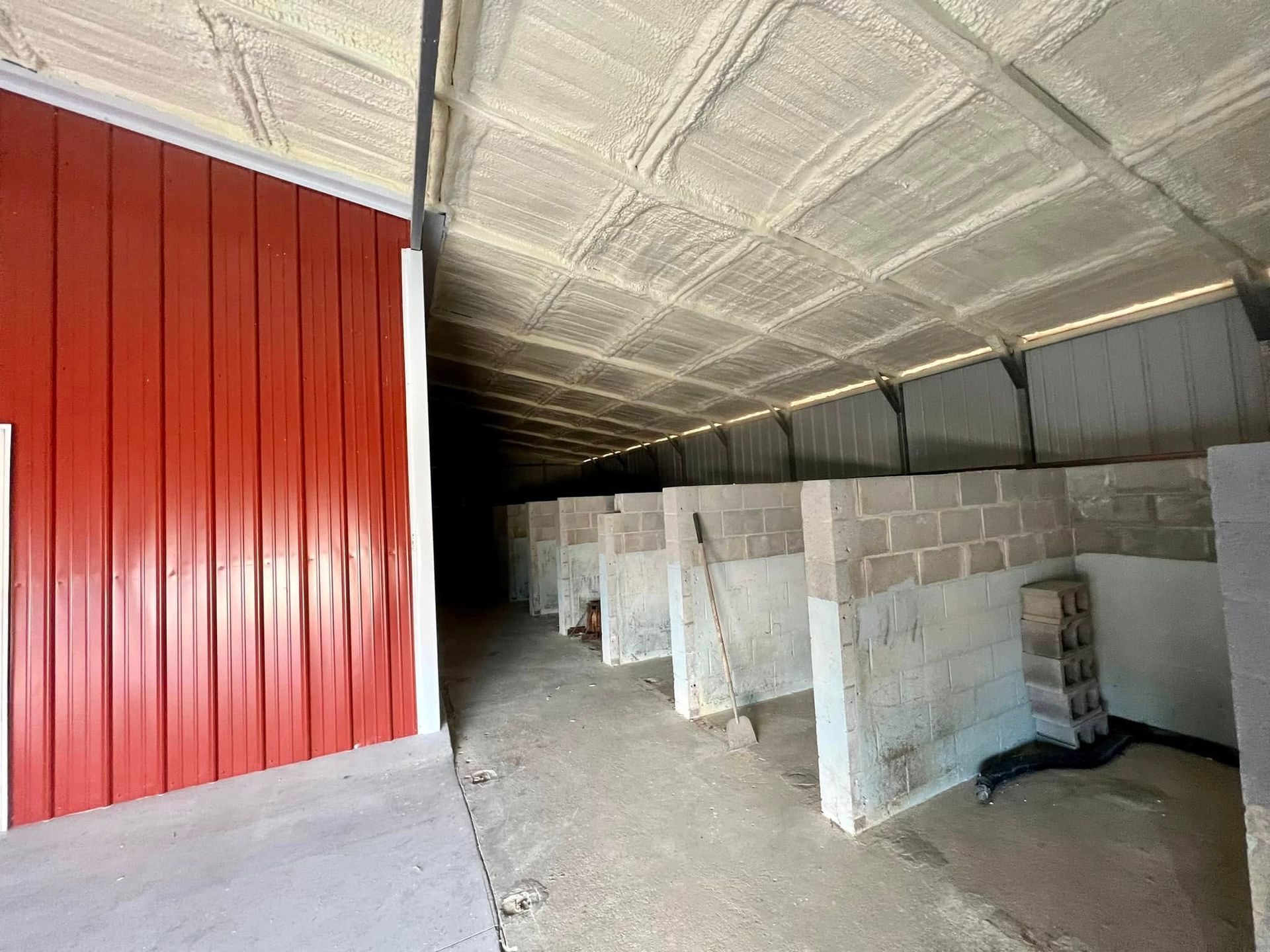 Red-walled interior with concrete block stalls, spray foam ceiling, and a dark hallway.
