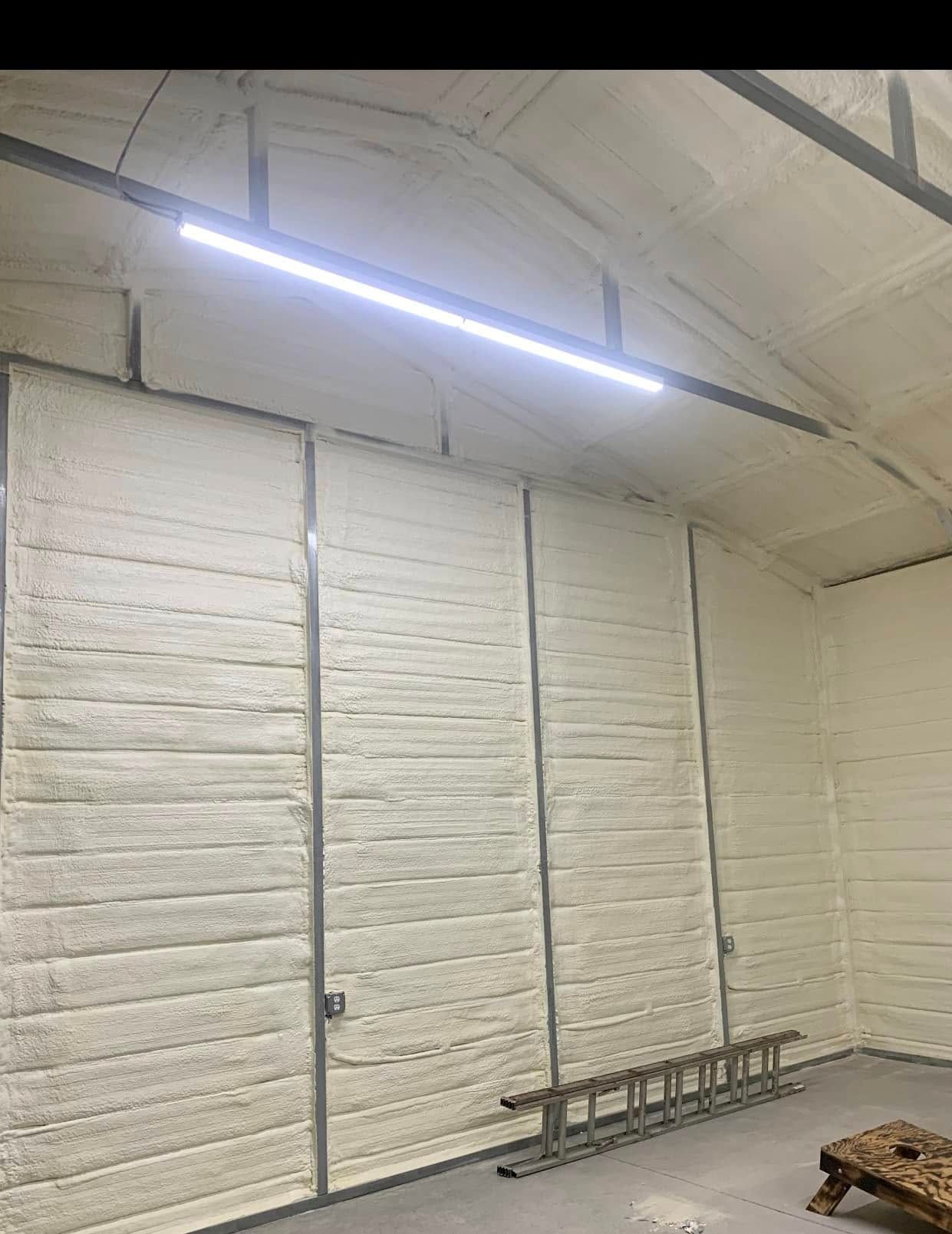 Interior of a building with white foam insulation on the walls. A linear light fixture is mounted on the ceiling.