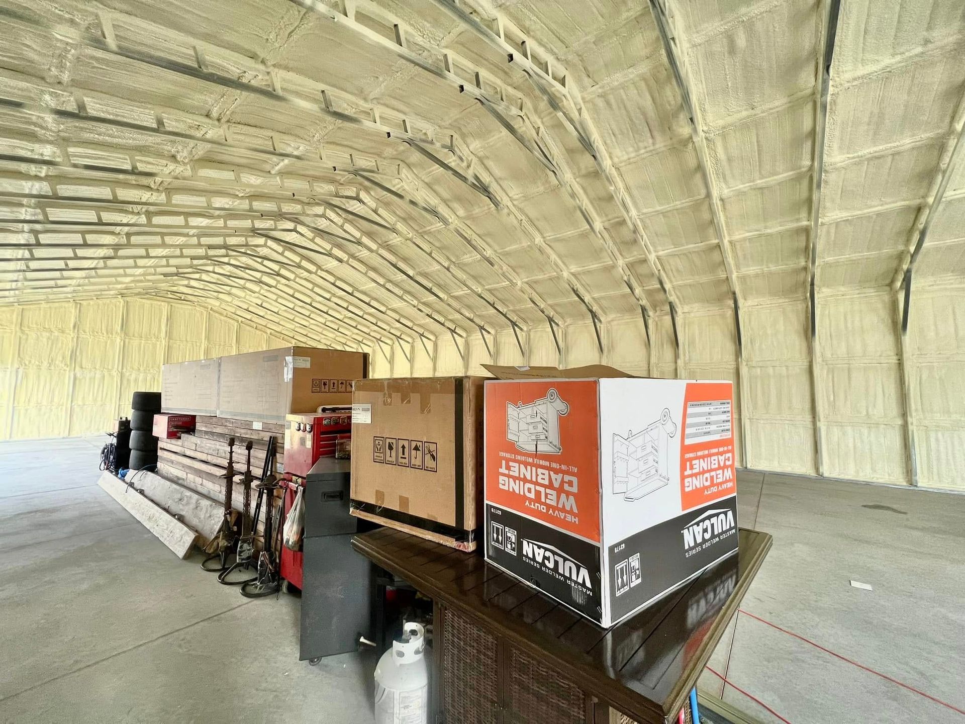 Interior of a warehouse with spray foam insulation. Boxes and equipment are visible on a table and floor.