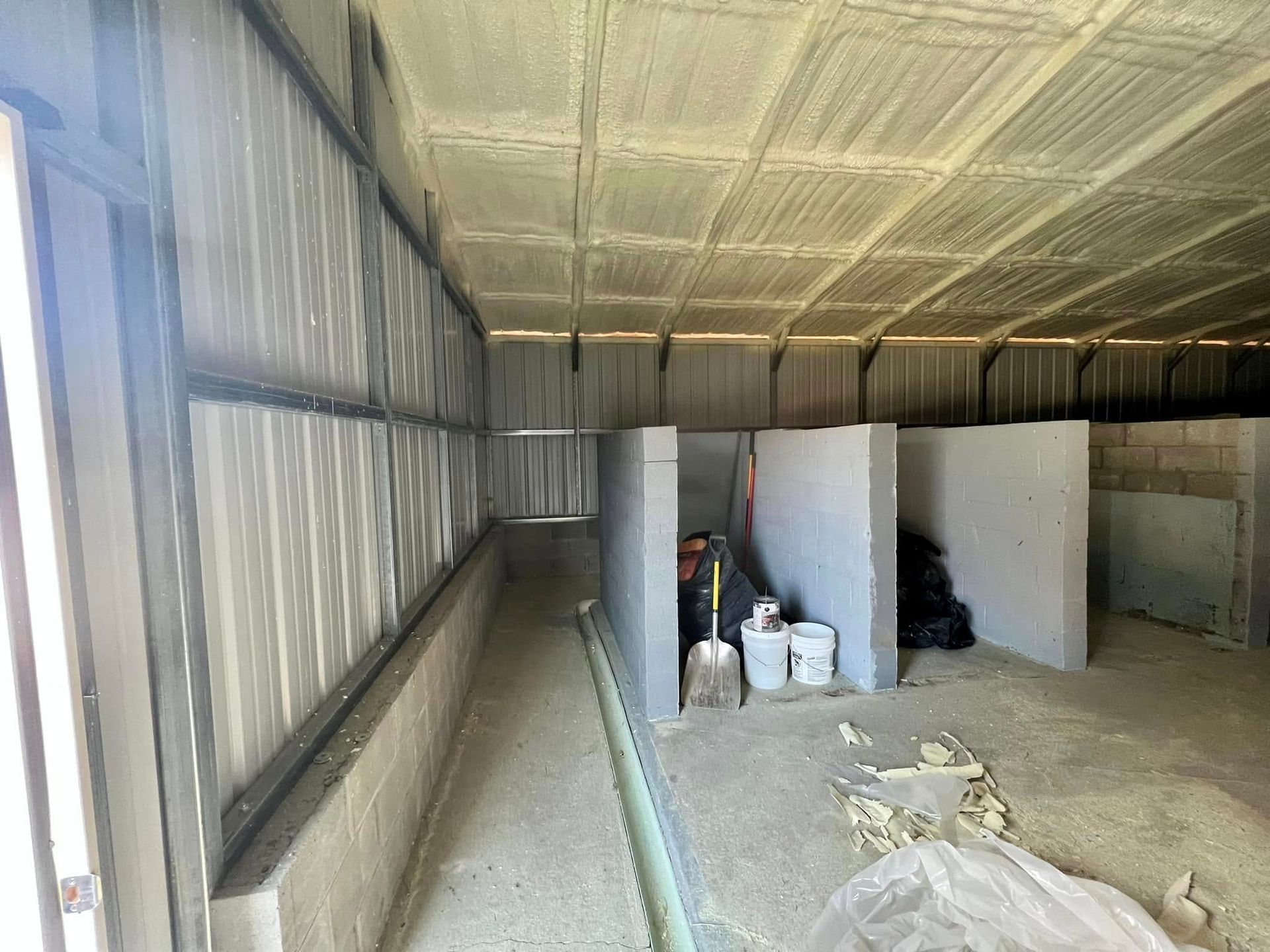 Interior of a metal building with concrete walls, small partition cubicles, and some tools and supplies.