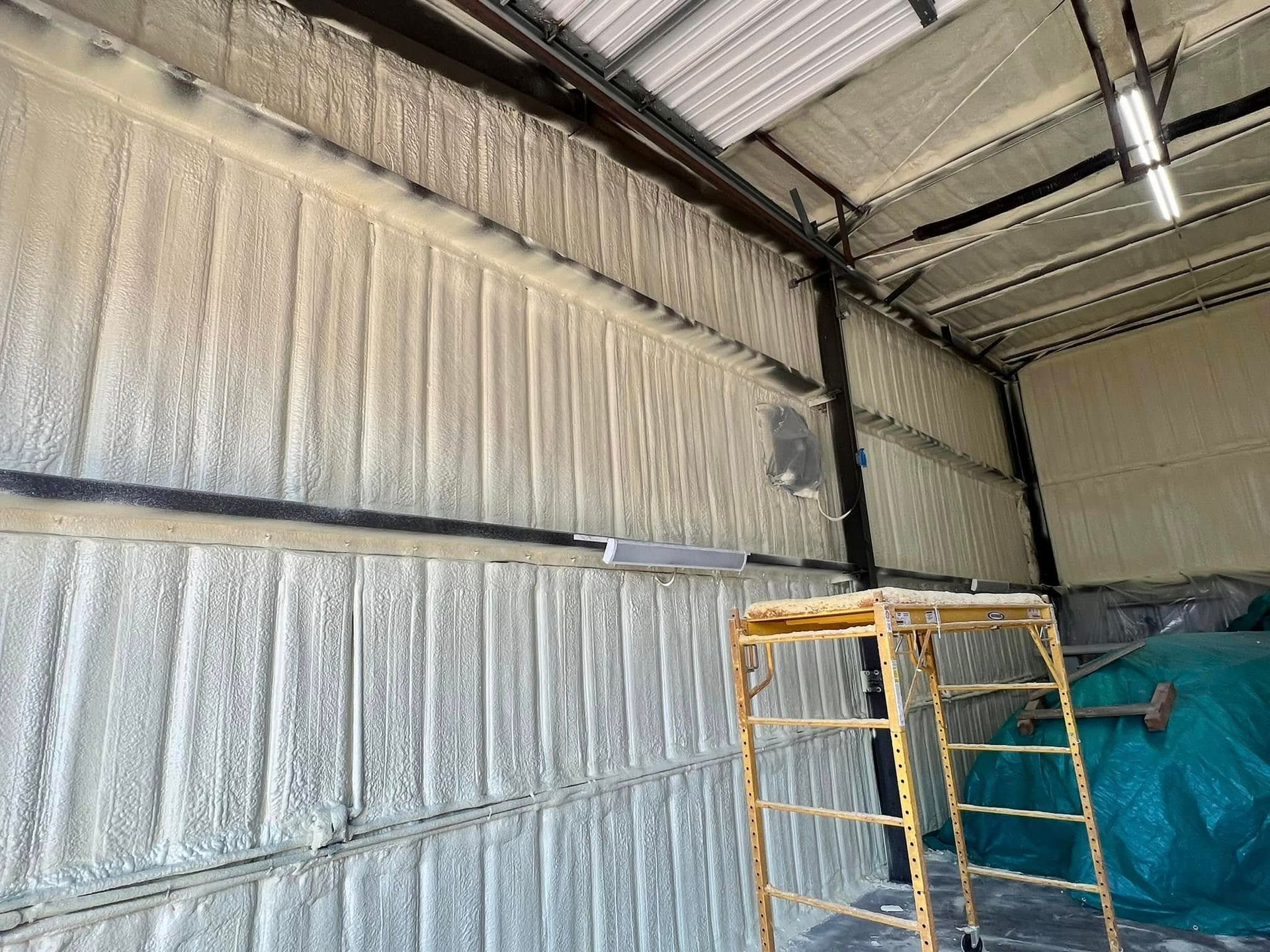 Interior view of a building with spray foam insulation on the walls and ceiling. A yellow scaffold is present.