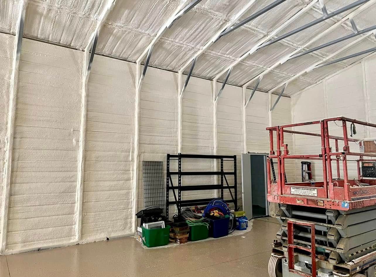 Interior view of a building with spray foam insulation on the walls and ceiling. A lift and shelving are present.