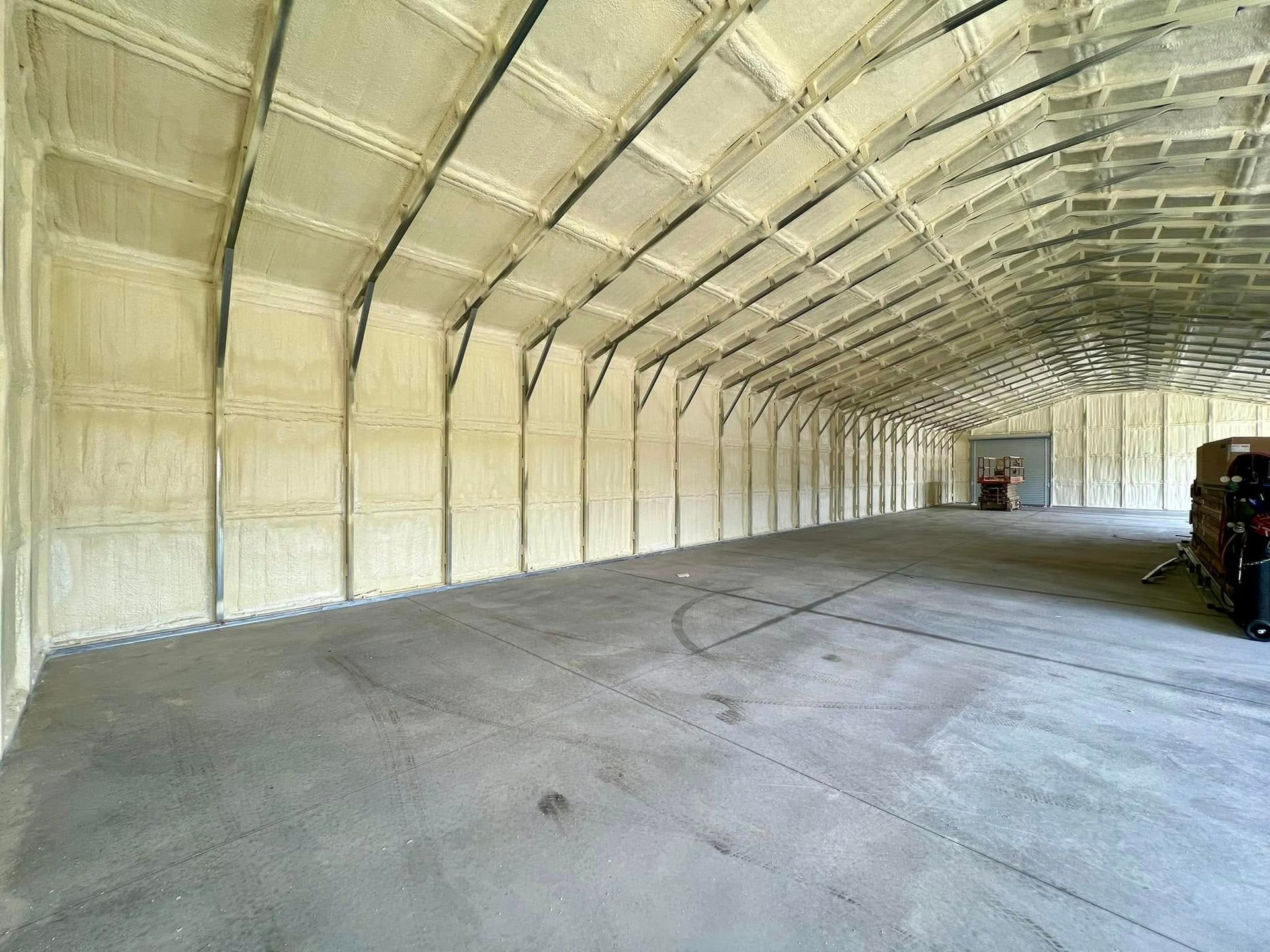 Interior of a large warehouse with spray foam insulation on walls and ceiling; concrete floor.