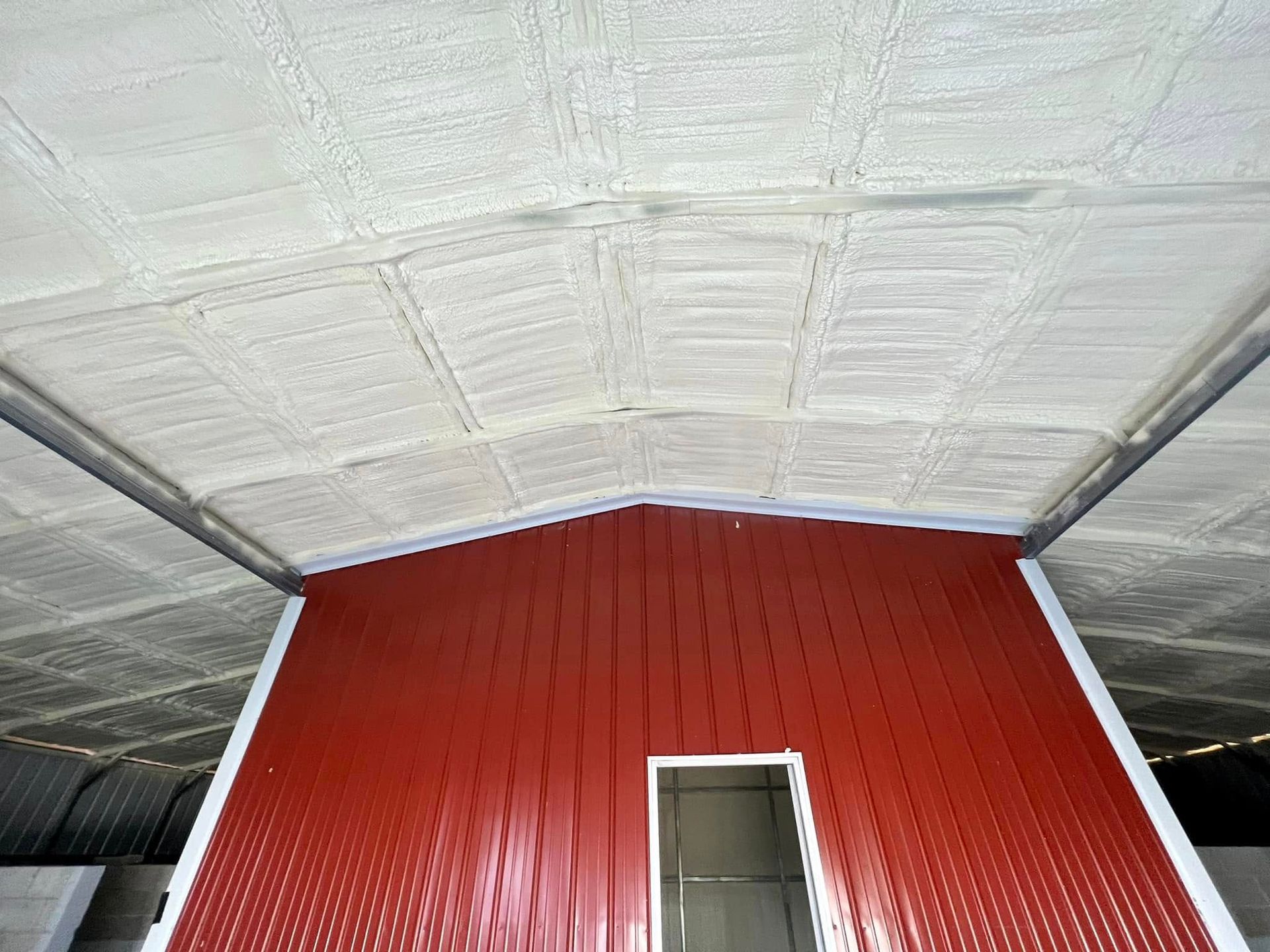 Interior of a building with red metal walls and a ceiling covered in white insulation.