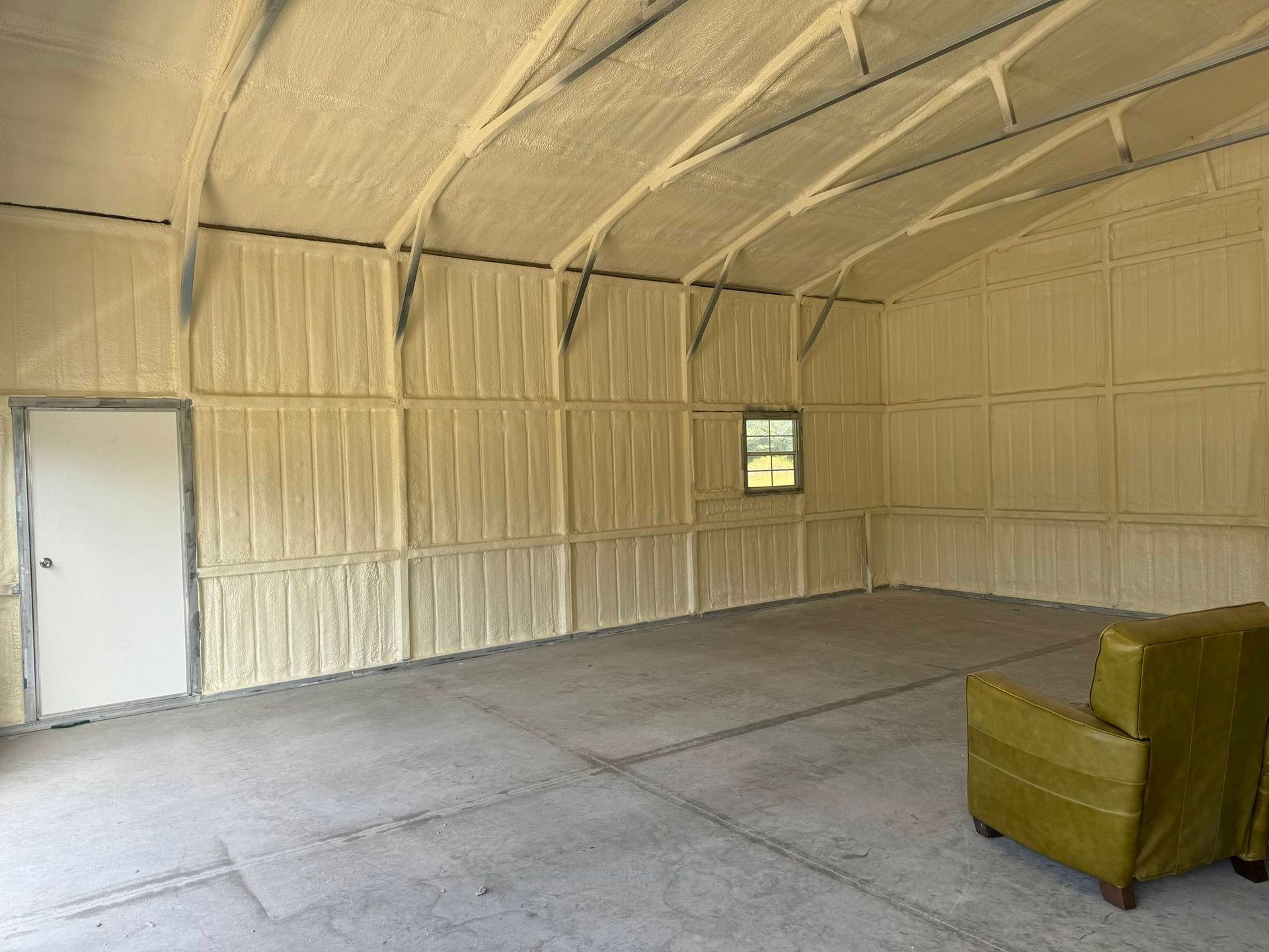 Interior of a building insulated with yellow spray foam, with a door, window, and green chair.