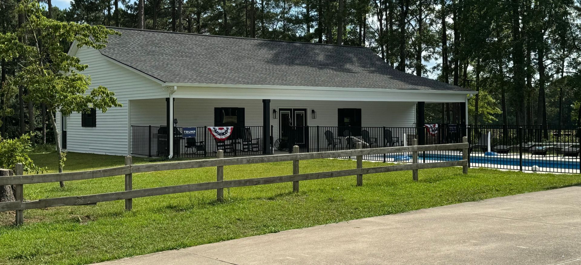 White house with a gray roof and a front porch, a fence, and a pool in the backyard.