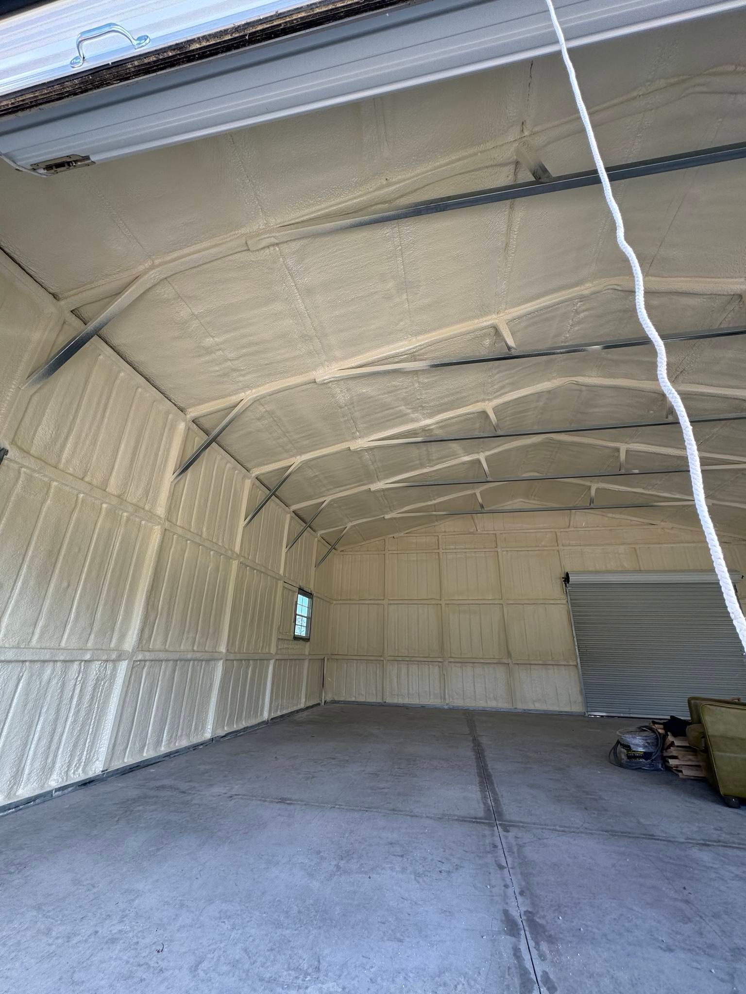 Interior view of a building insulated with spray foam. Light beige foam covers the walls and ceiling, gray floor.