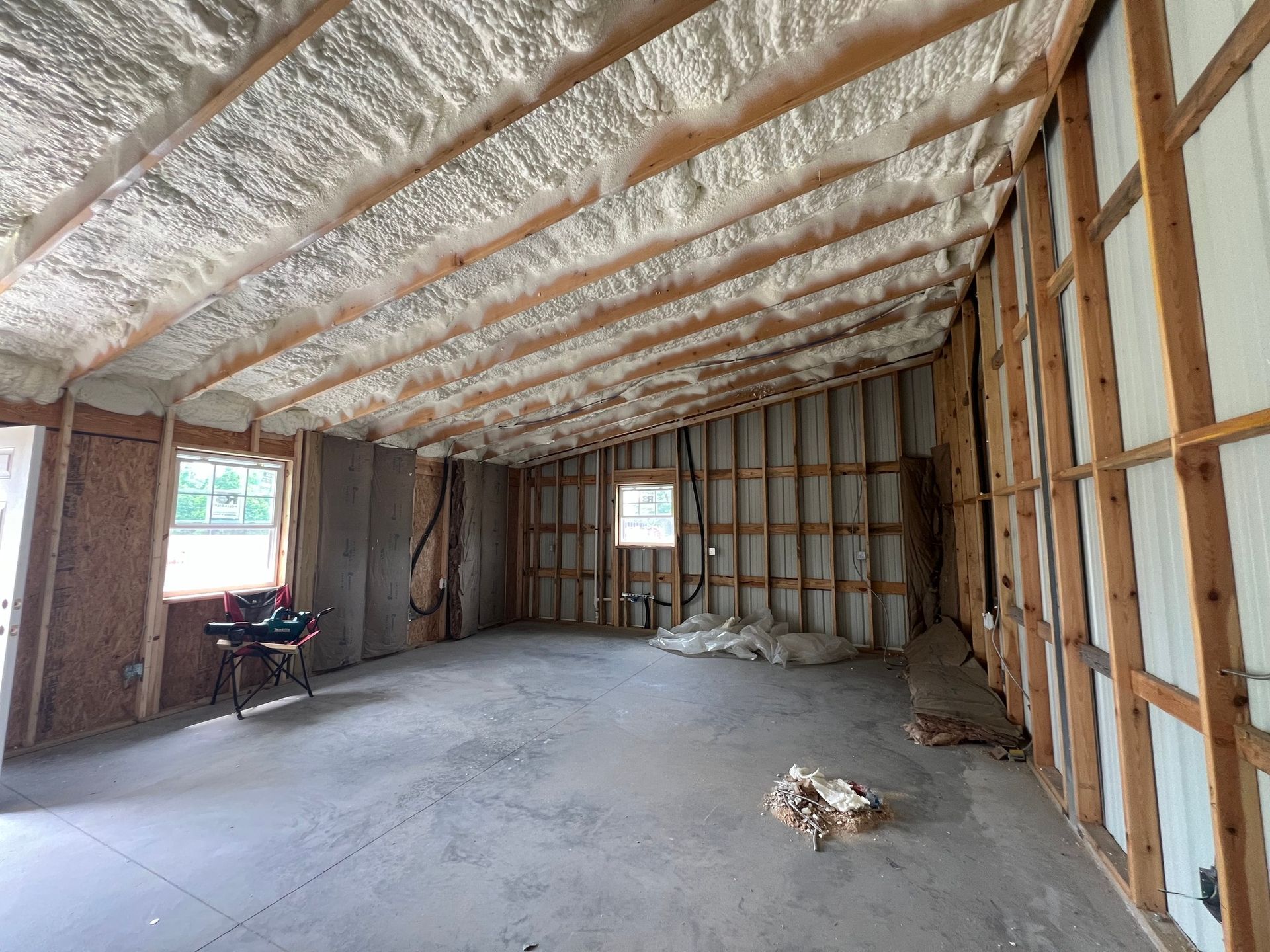 Interior of a room with exposed wooden framing and spray foam insulation on the ceiling. Concrete floor.