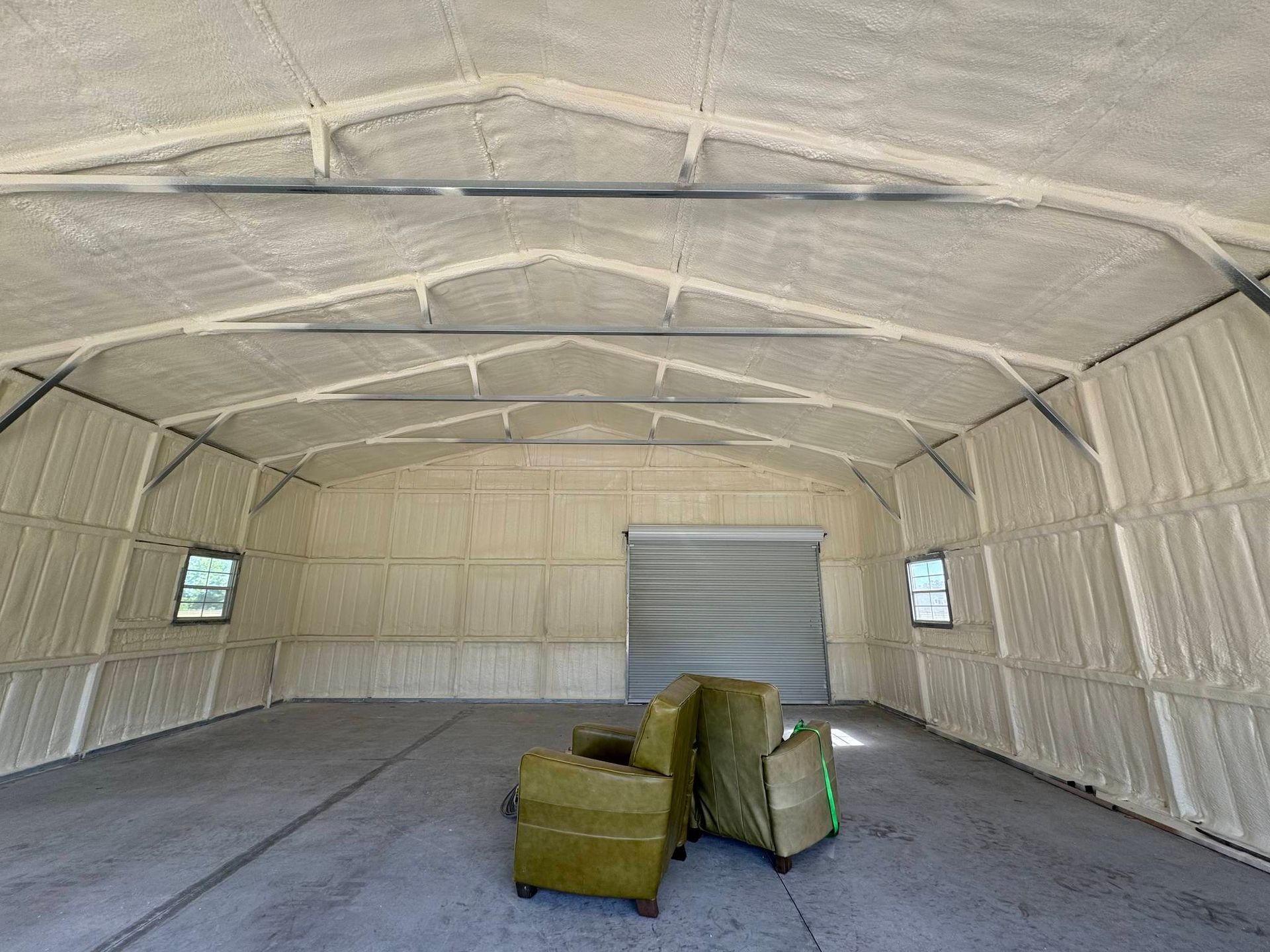 Interior view of a building with spray foam insulation on the walls and ceiling. A closed garage door is in the back.