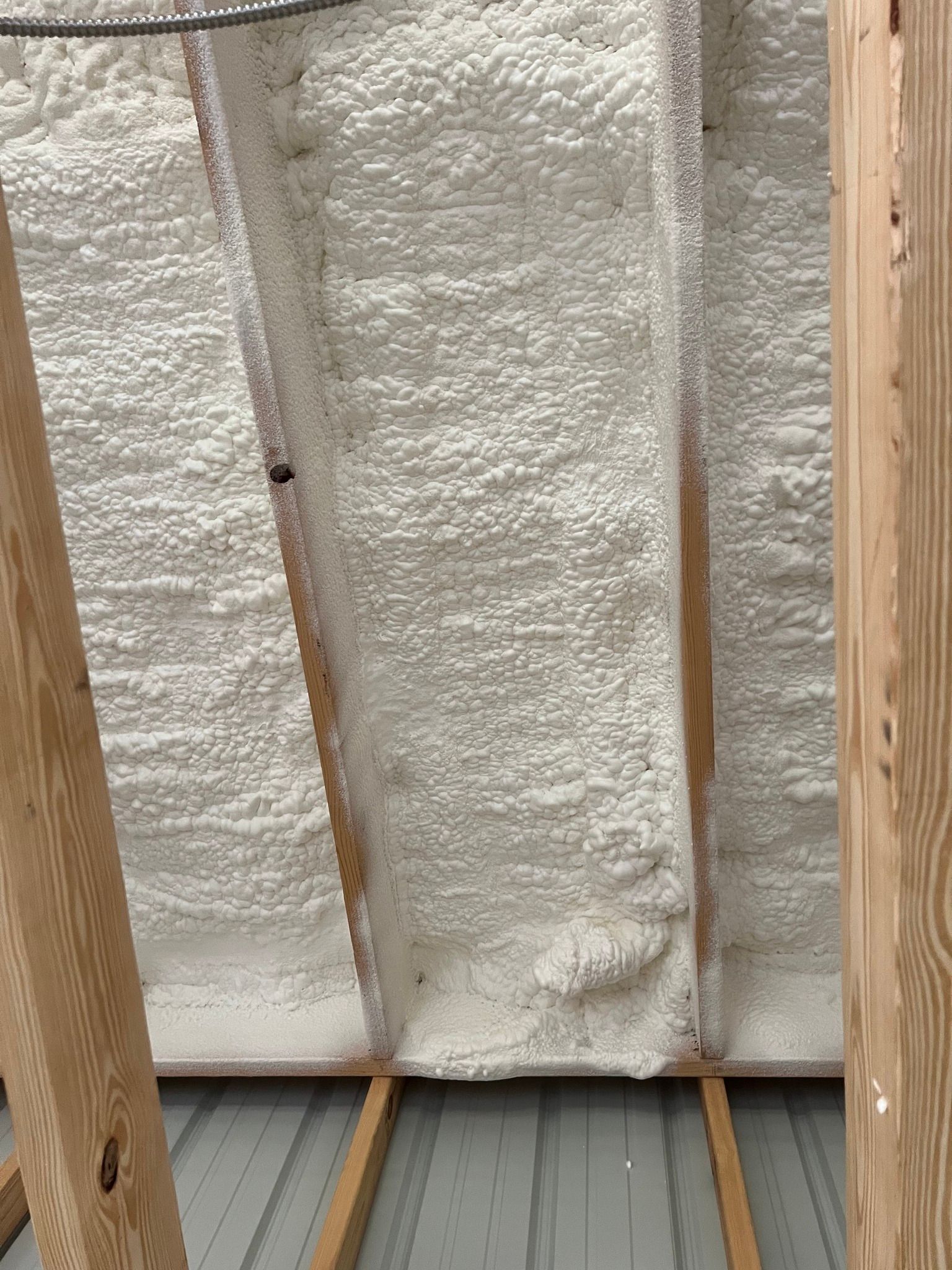 White spray foam insulation fills the space between wooden rafters in an attic.