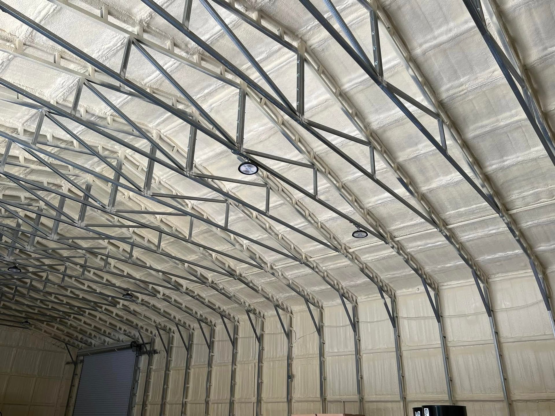 Interior of a building with arched metal framework. Insulation coats walls and ceiling. Two lights are visible.