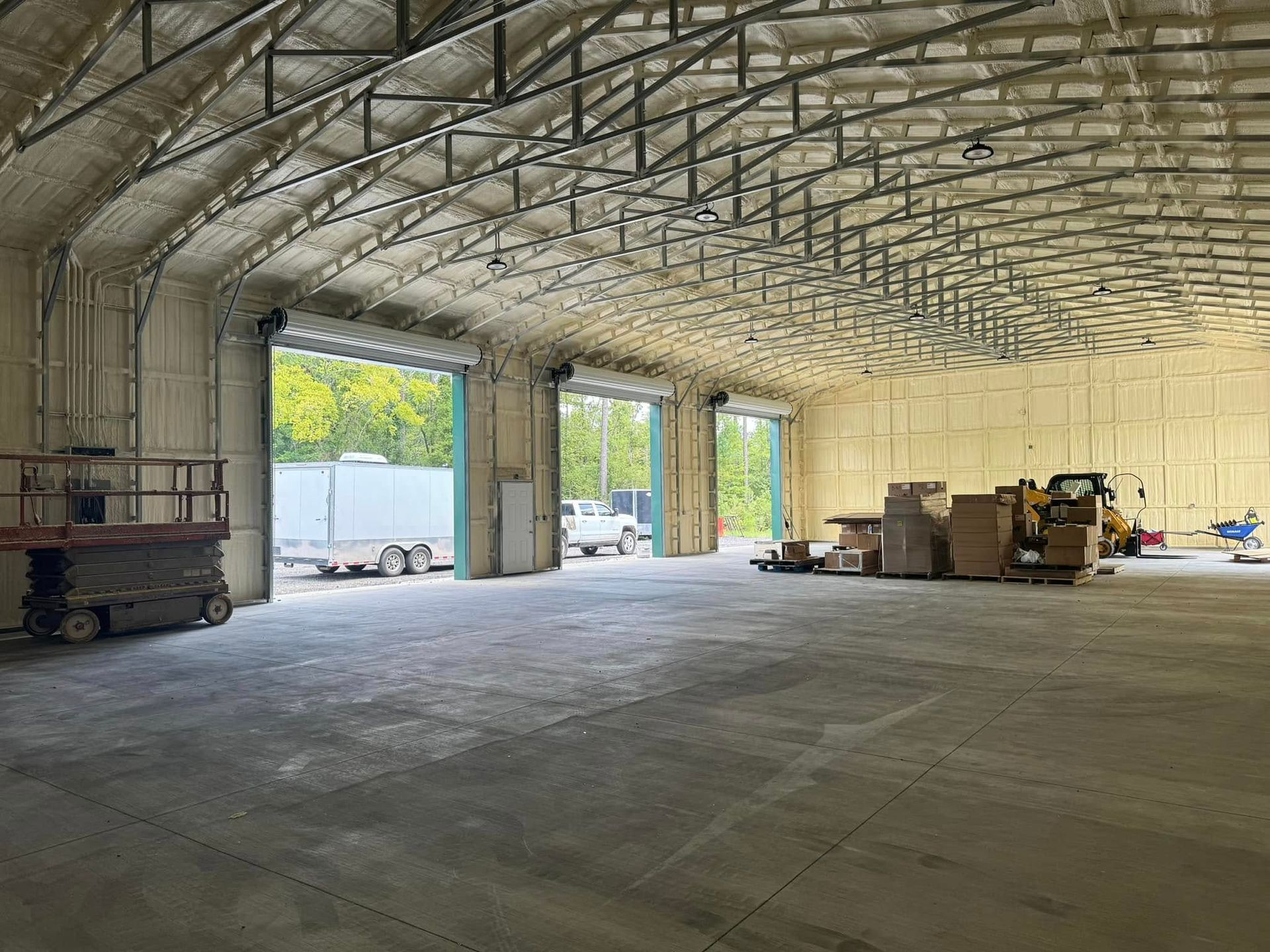 Inside a large warehouse with three open bay doors, spray foam insulation, and construction equipment.